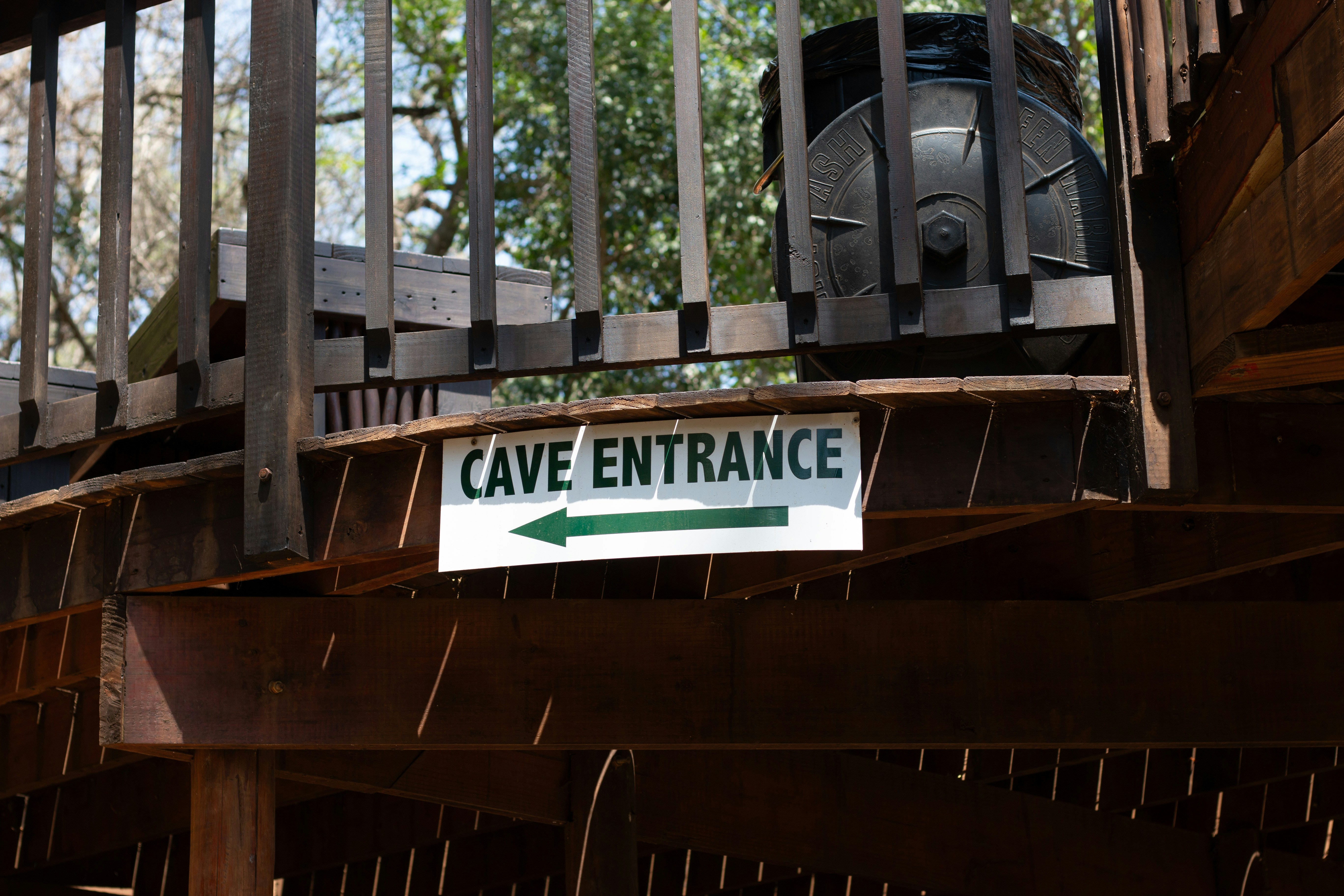 A sign reading CAVE ENTRANCE with a green arrow under a wooden deck