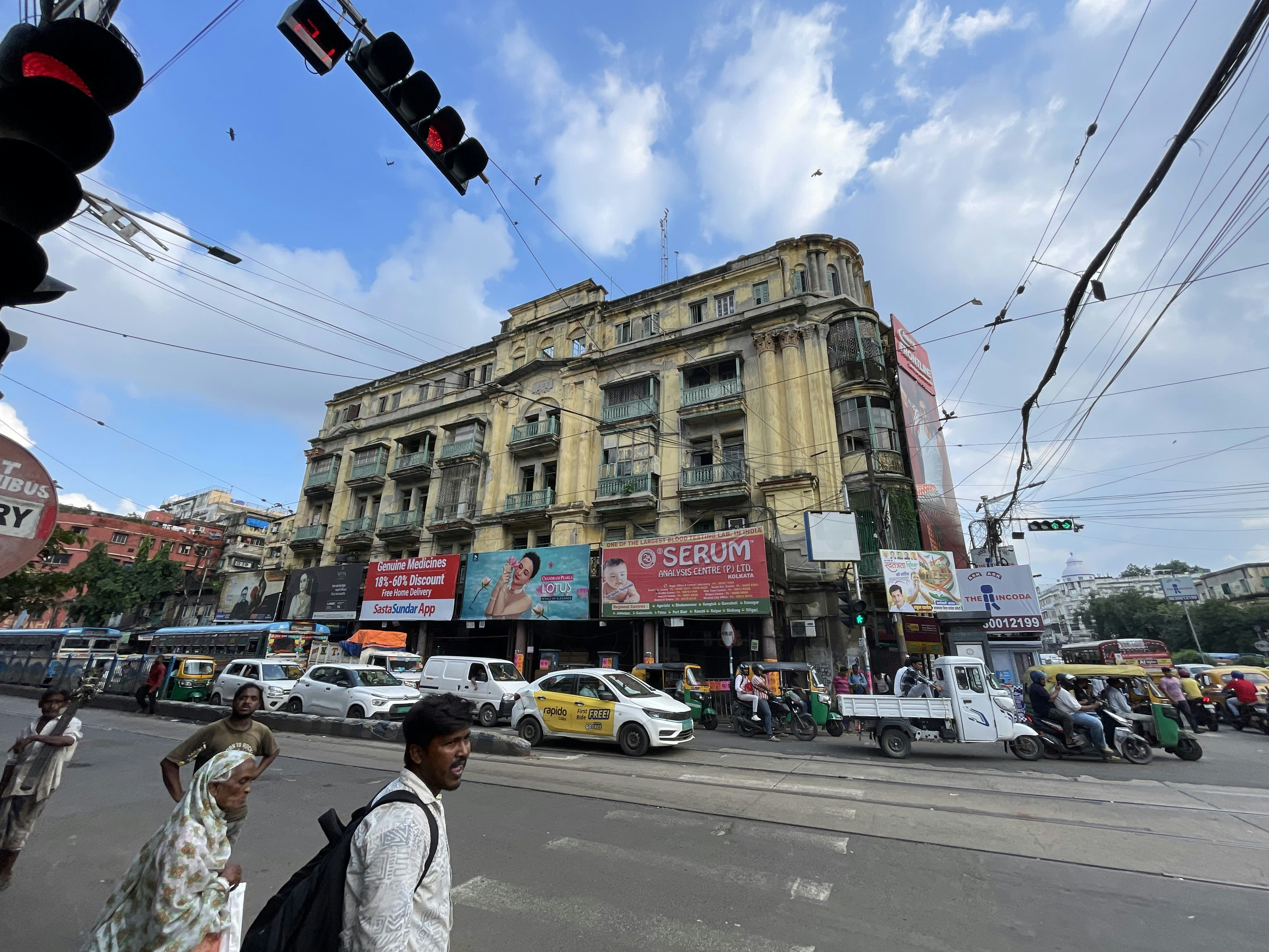 People walking on a busy street in front of a weathered yellow building in Kolkata