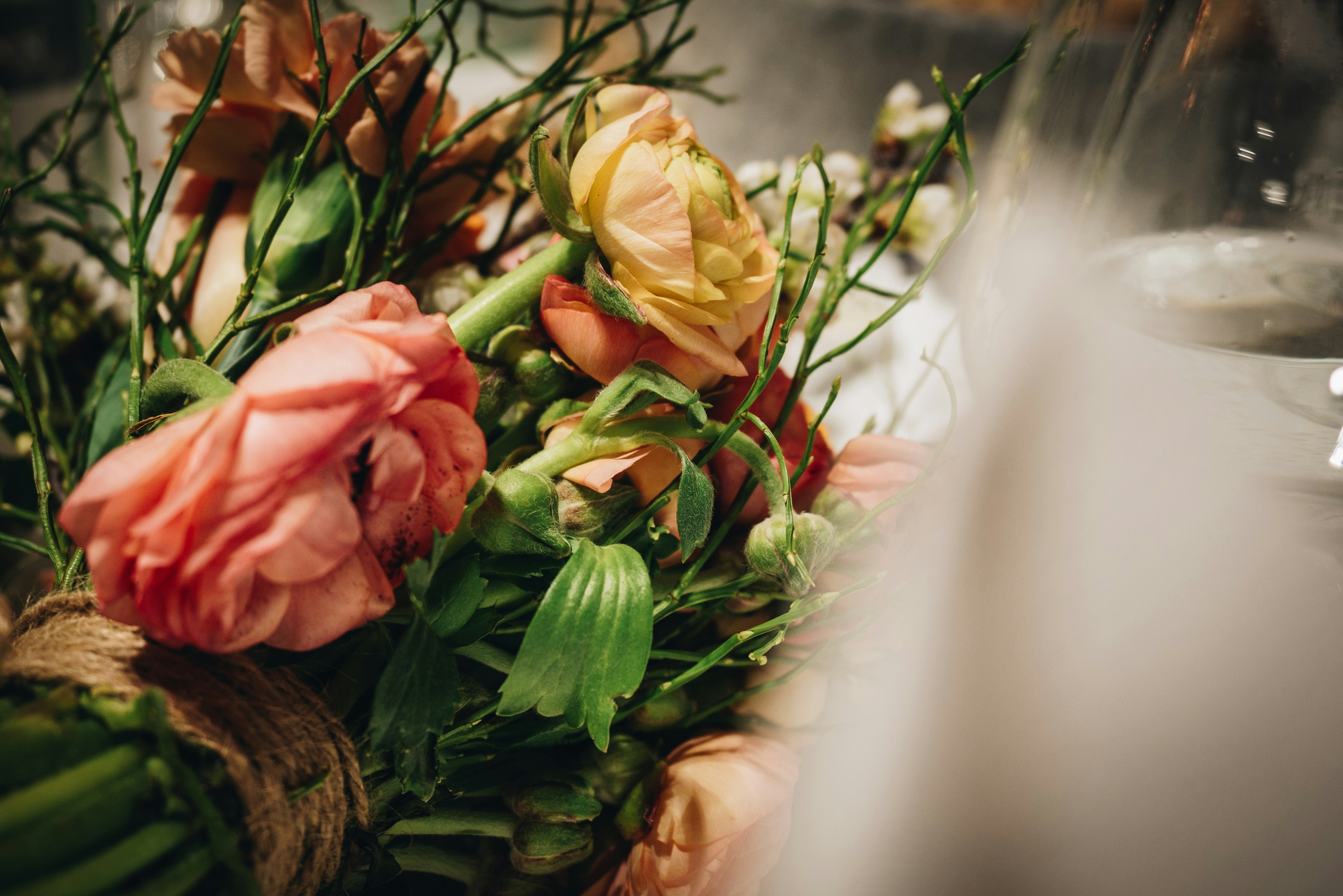 A bouquet of peach and pink ranunculus flowers tied with rustic twine