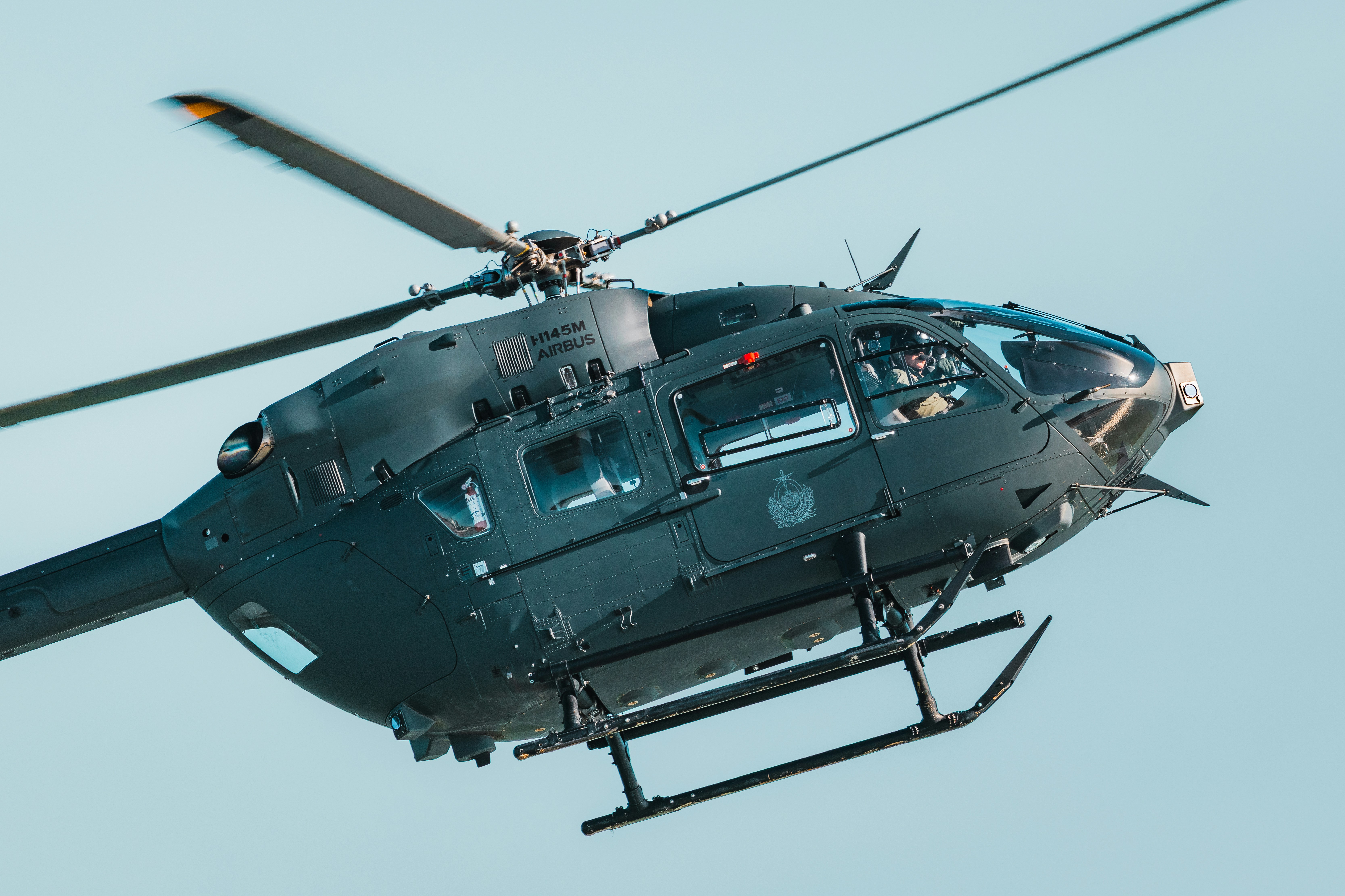 Helikopter militer hijau tua terbang melawan langit biru terang yang cerah