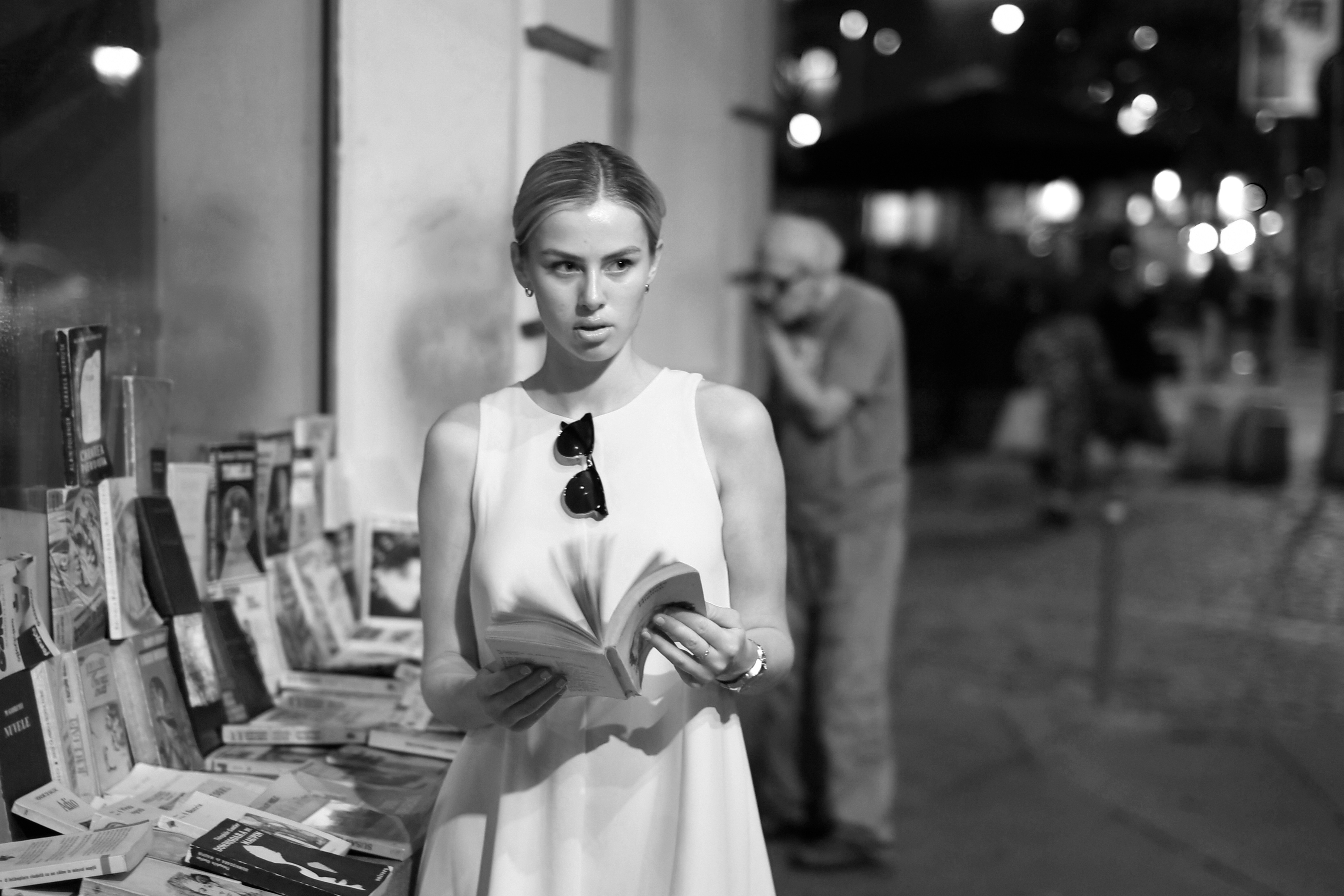 A woman in a white dress reading a book at an outdoor bookstall
