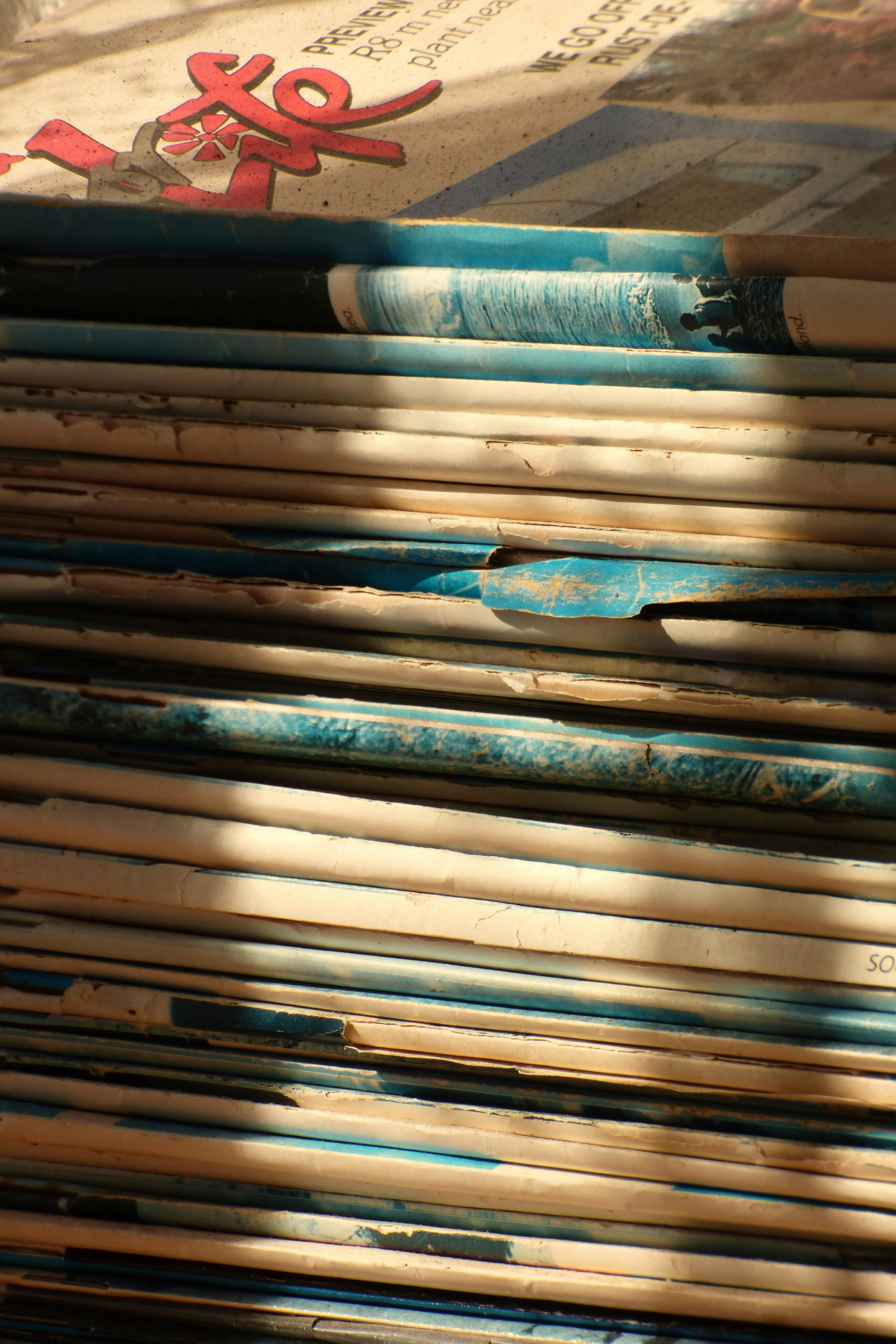 A tall stack of weathered magazines seen from the spines