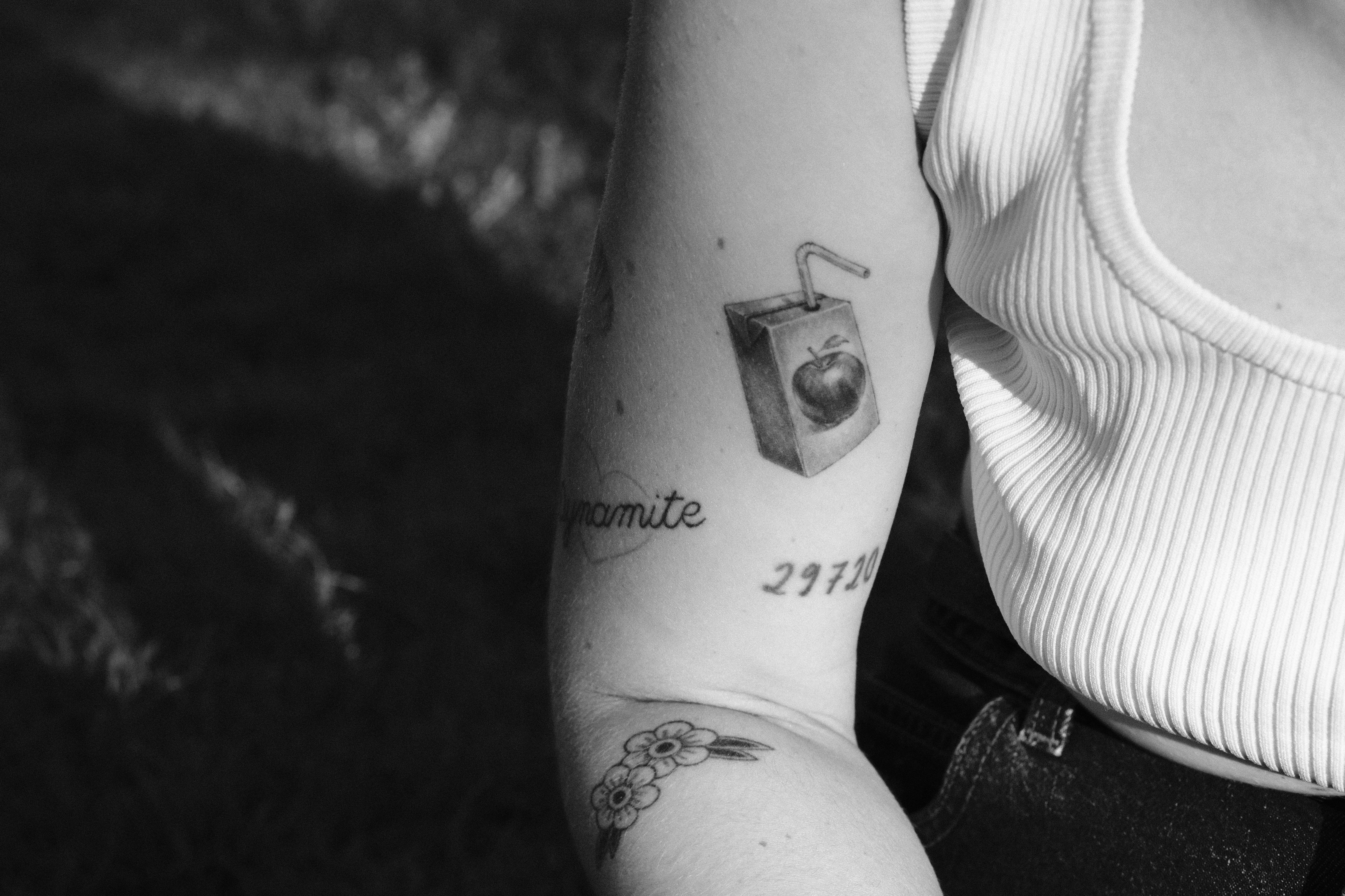 A person with multiple tattoos on their arm including a juice box