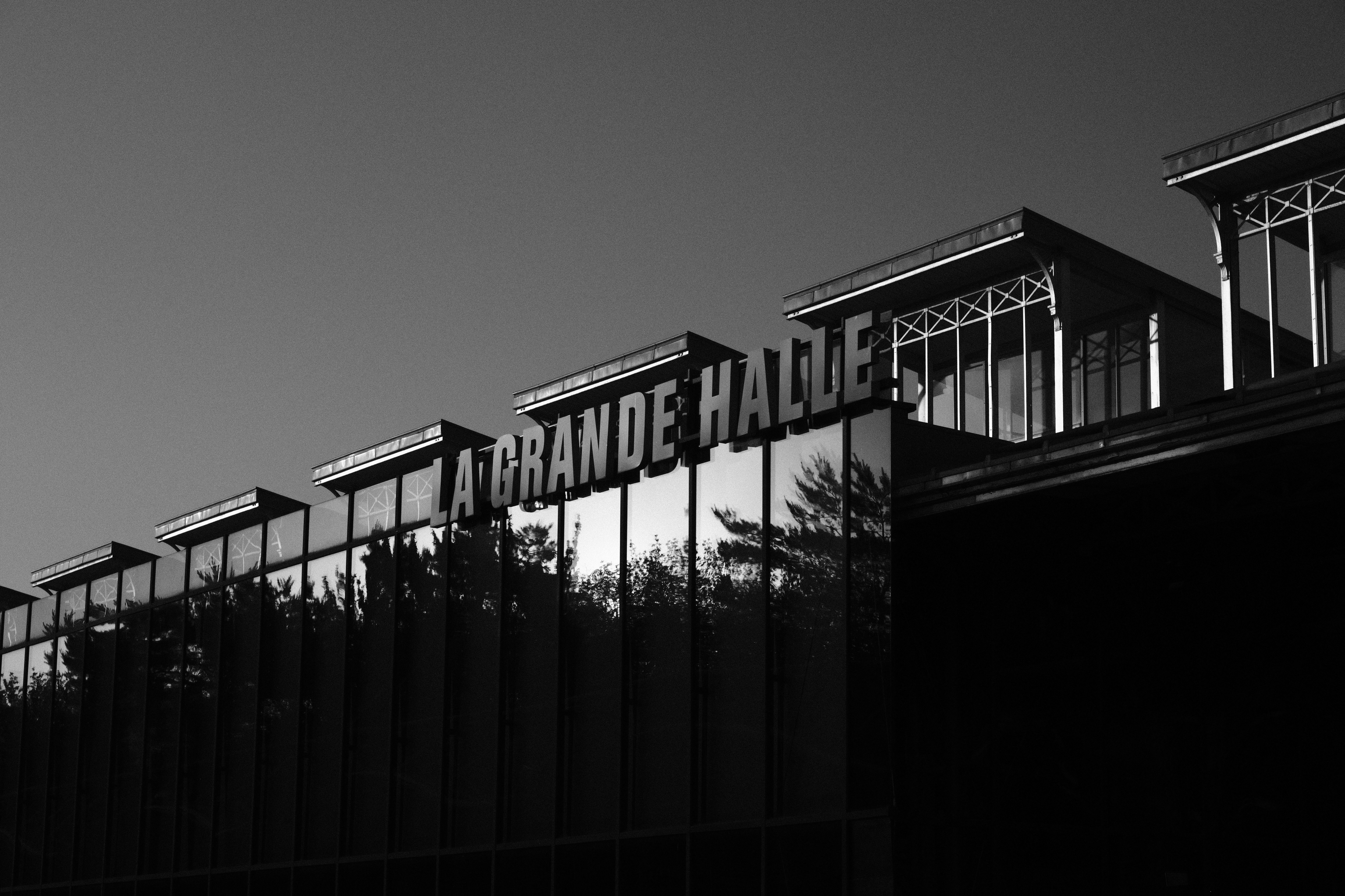 The glass facade of La Grande Halle with trees reflected in the windows