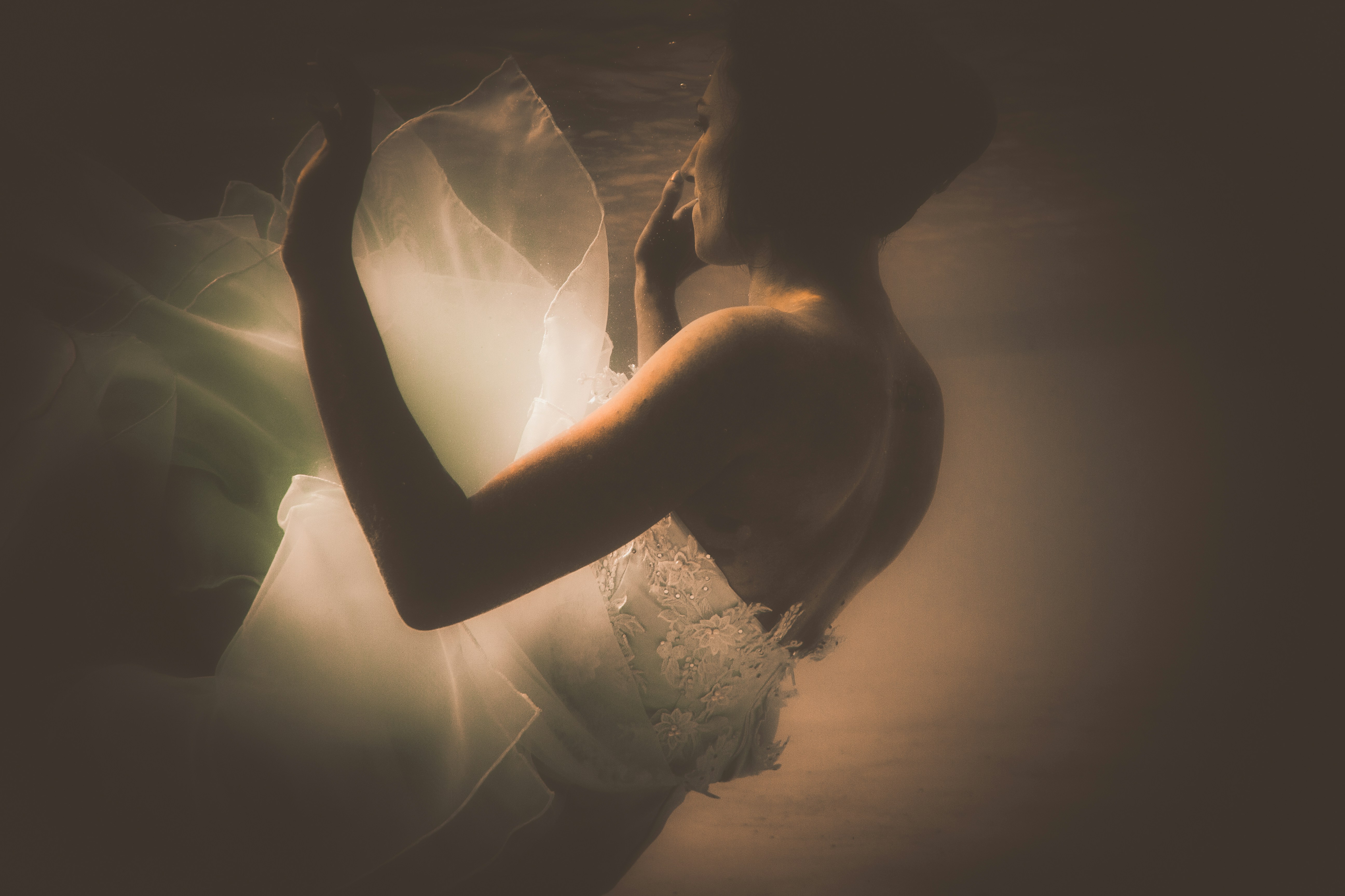 A woman in a white lace dress floating underwater with flowing fabric