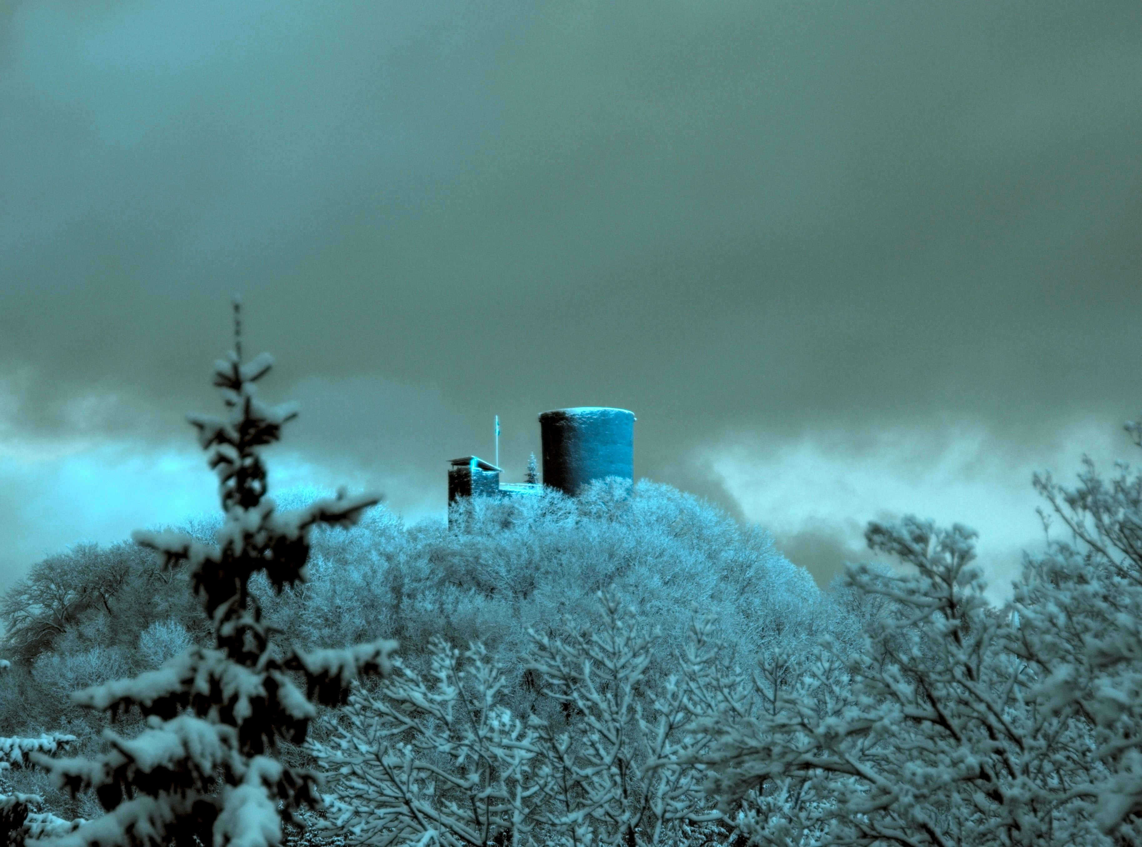 A stone tower on a snow-covered hill surrounded by frosted trees under a dark sky