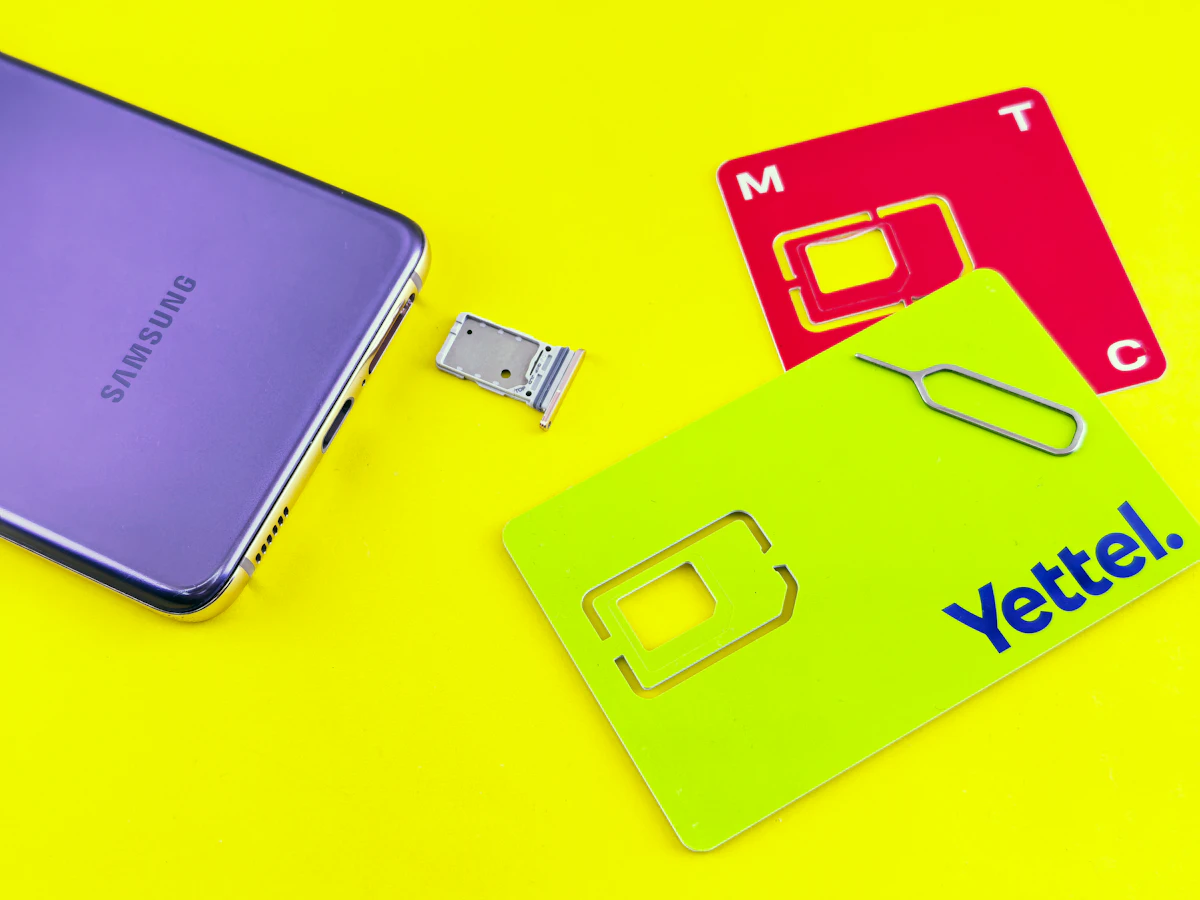 Ponsel ungu, baki SIM, dan dua kartu SIM di atas permukaan kuning