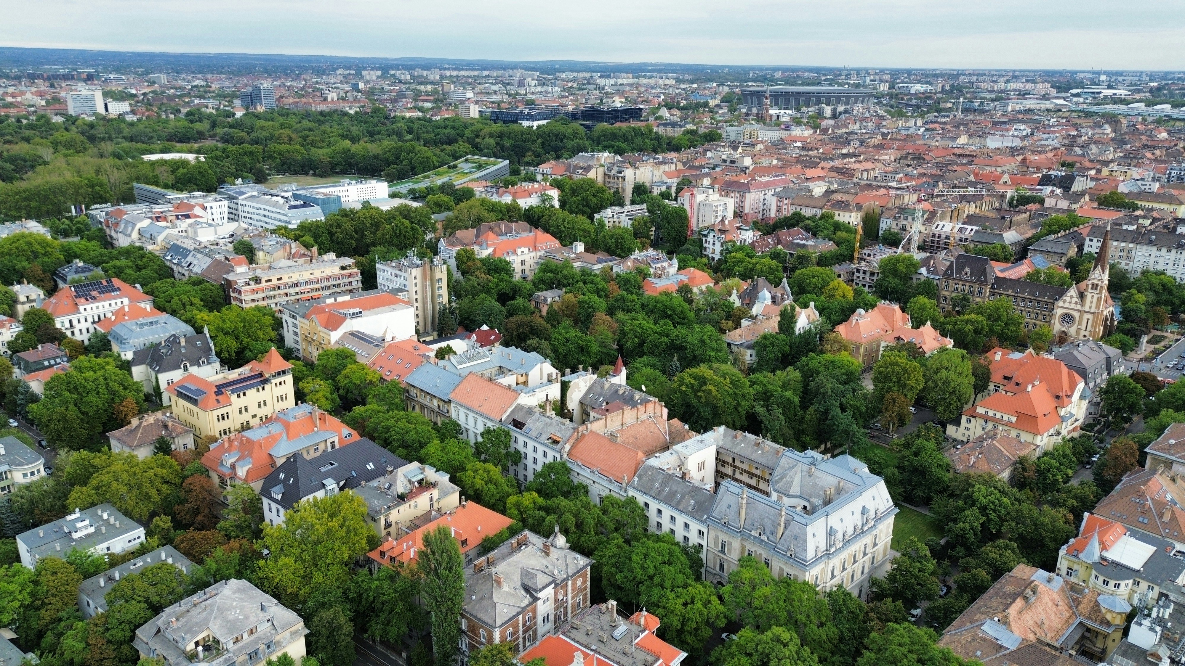 Aerial view of a dense city with red roofs and green trees in Budapest
