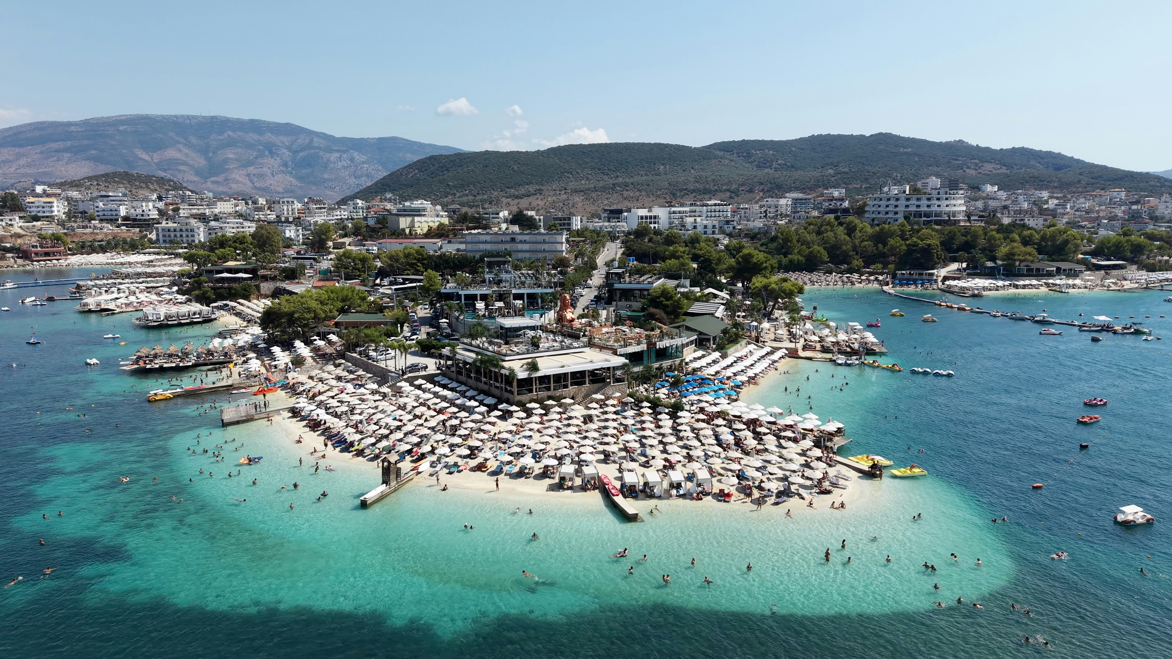 Aerial view of a crowded beach with white umbrellas on a turquoise bay