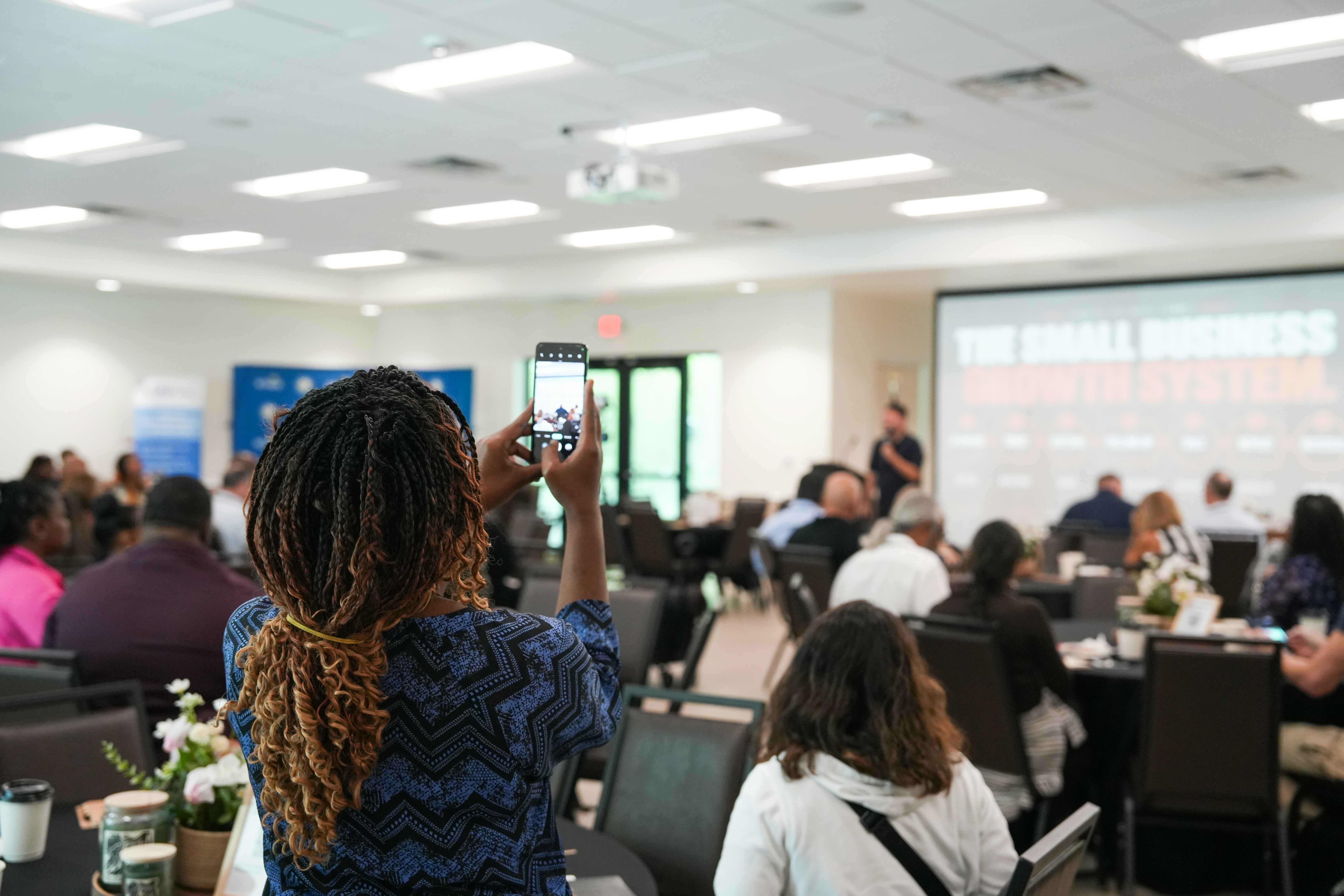 A person with braided hair photographing a business presentation with a smartphone