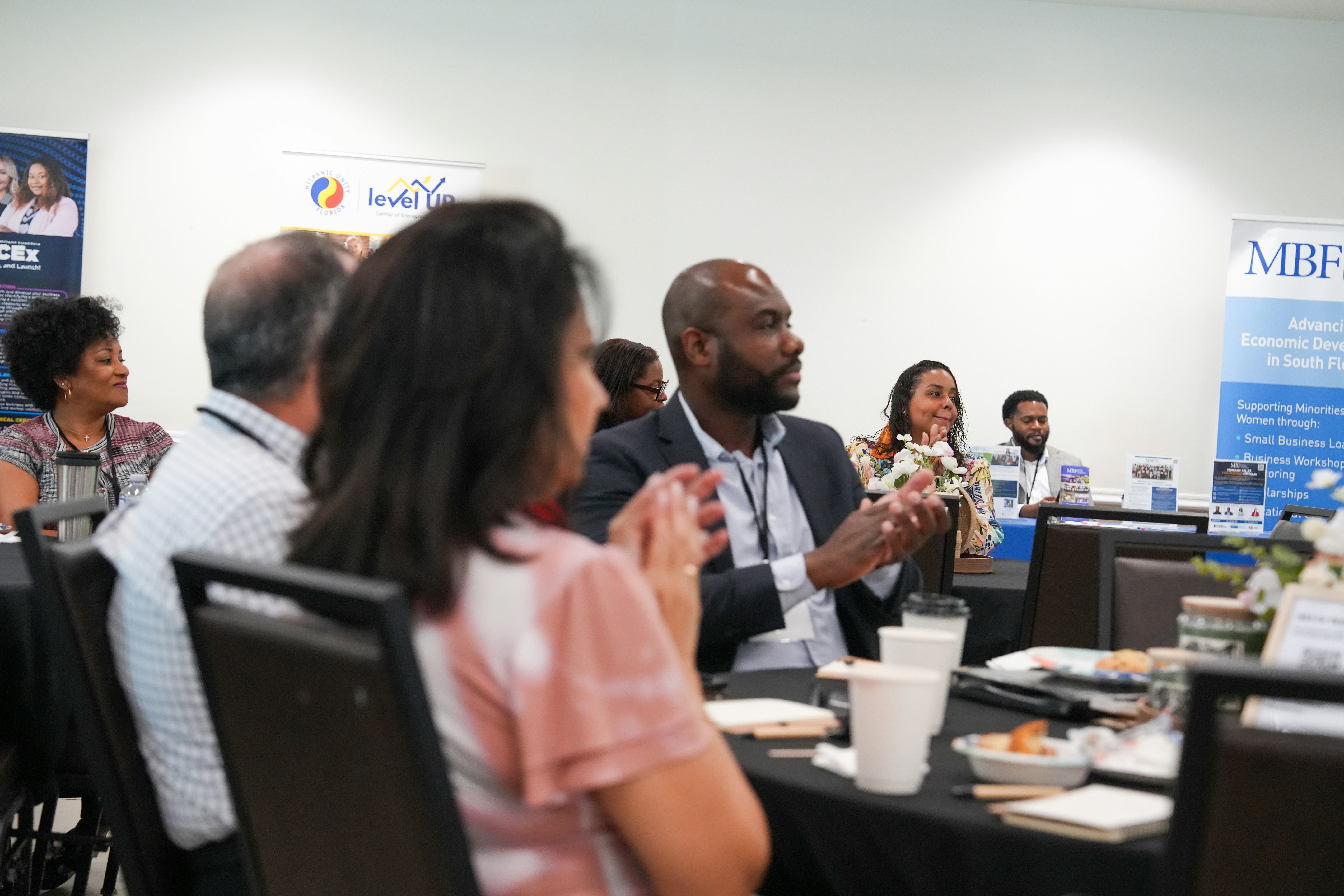 A group of people clapping at a business conference with branded banners