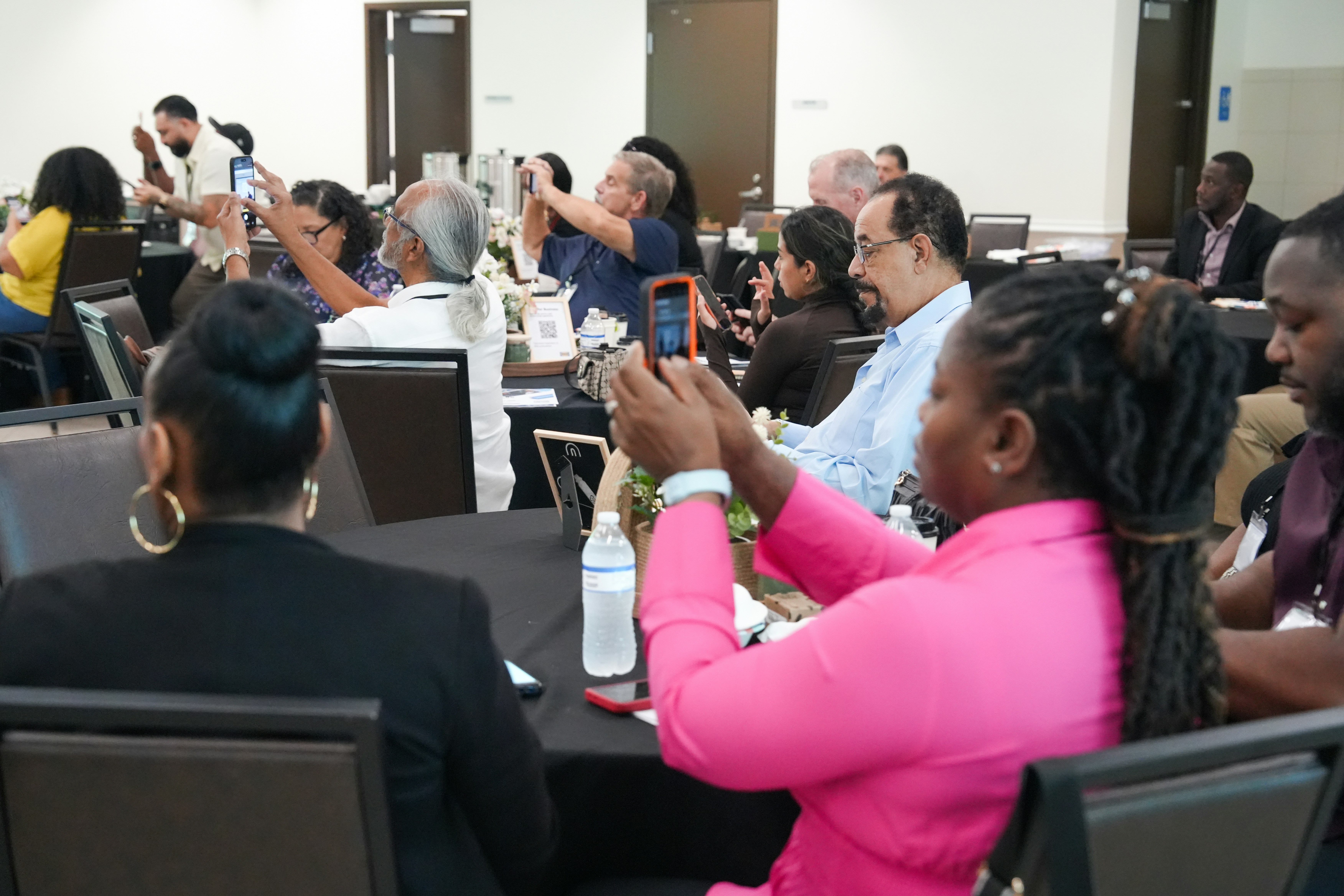 People at tables in a conference room holding up smartphones to take photos