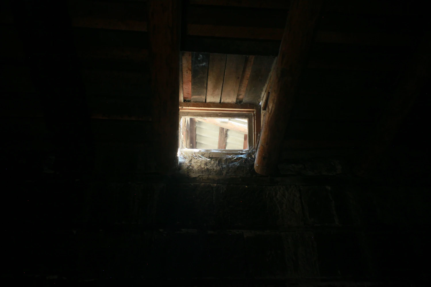 A small bright window set high in a dark stone wall under heavy ceiling beams