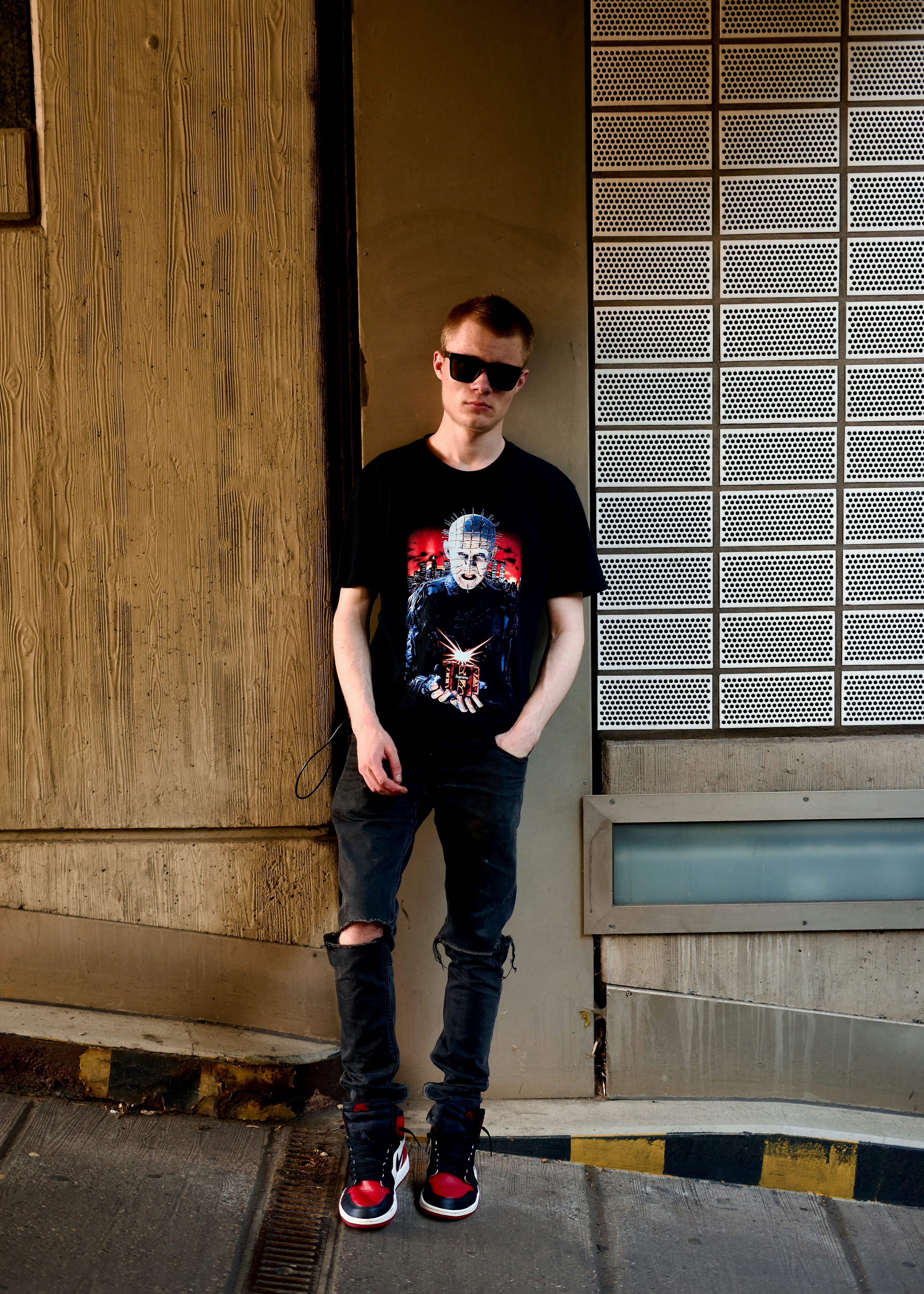 A person in sunglasses and a graphic t-shirt leaning against a textured wall