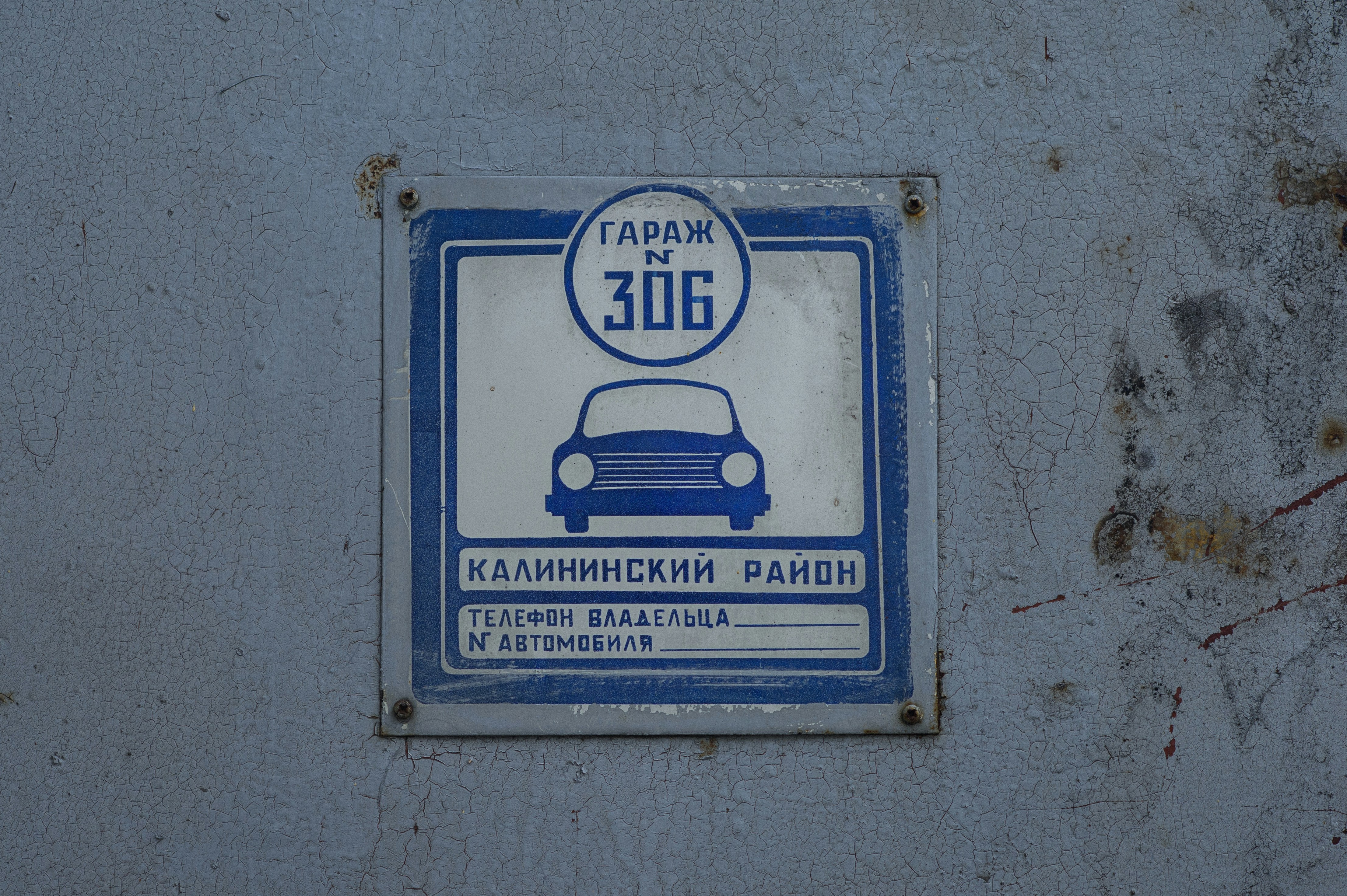 Un cartel metálico azul y blanco para el número 306 del garaje en una pared desgastada