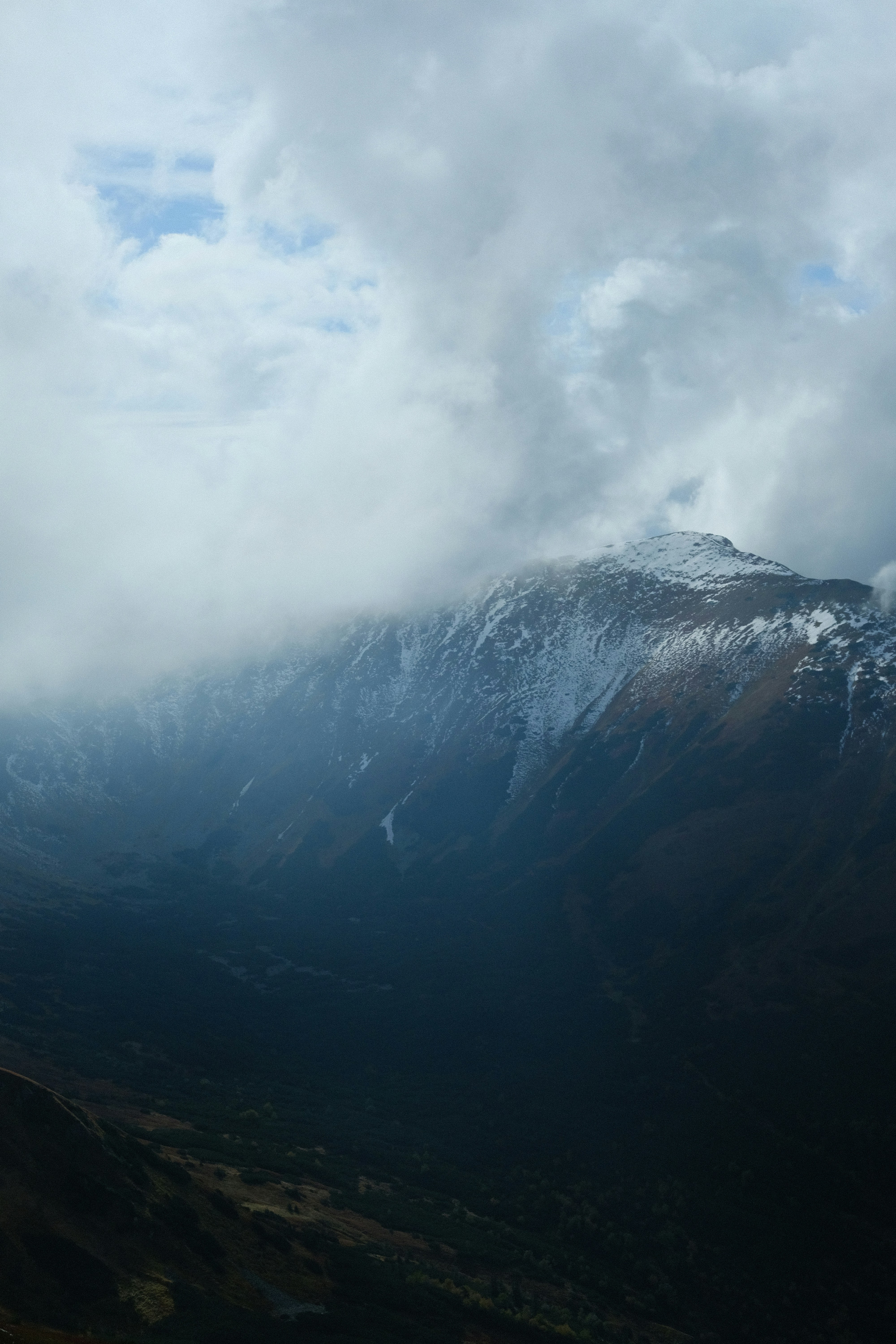 A snow-capped mountain peak partially obscured by thick white clouds