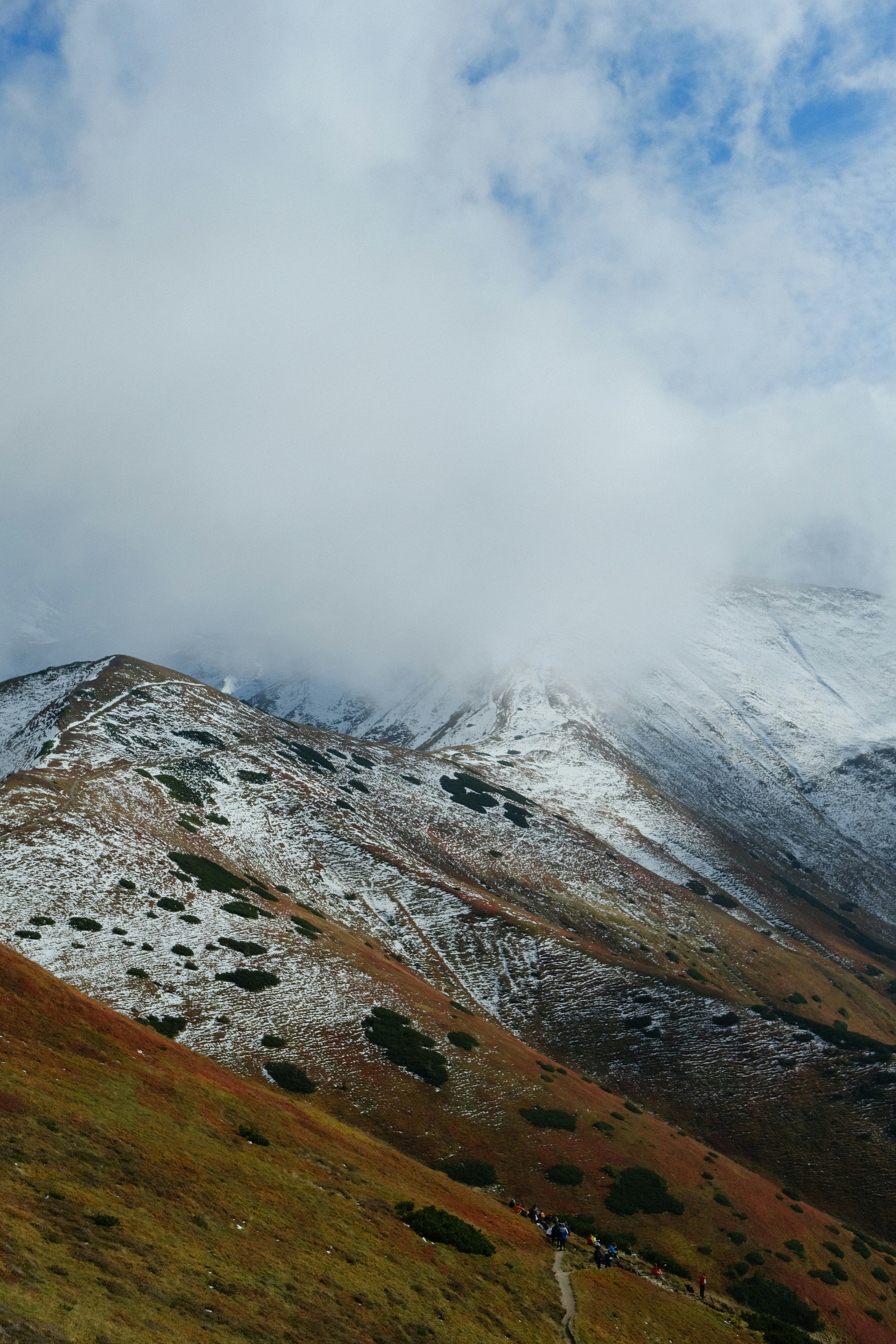 A group of people hiking on a trail up a snow-dusted mountain slope