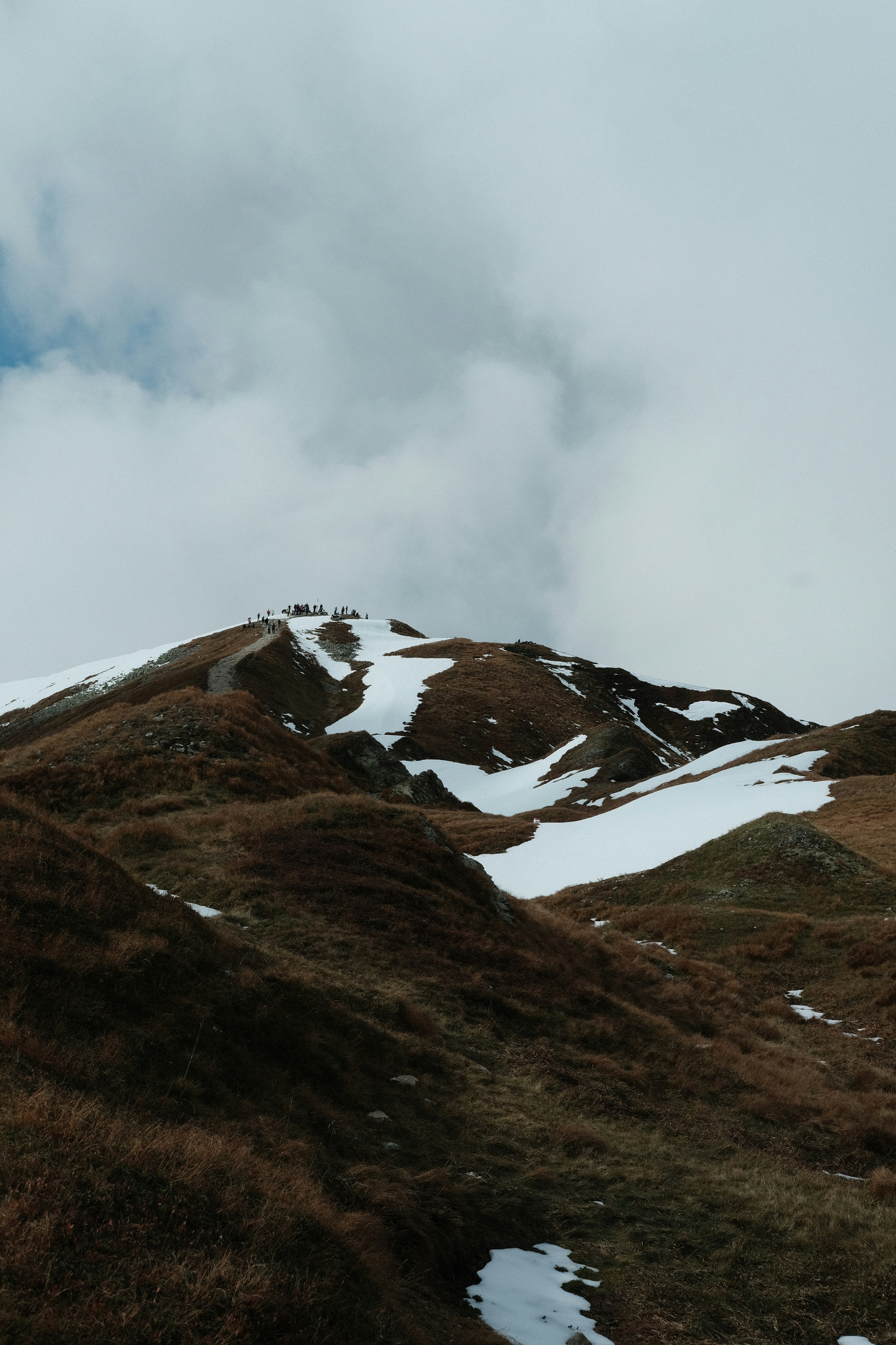 A group of people on a snowy mountain peak under a cloudy sky