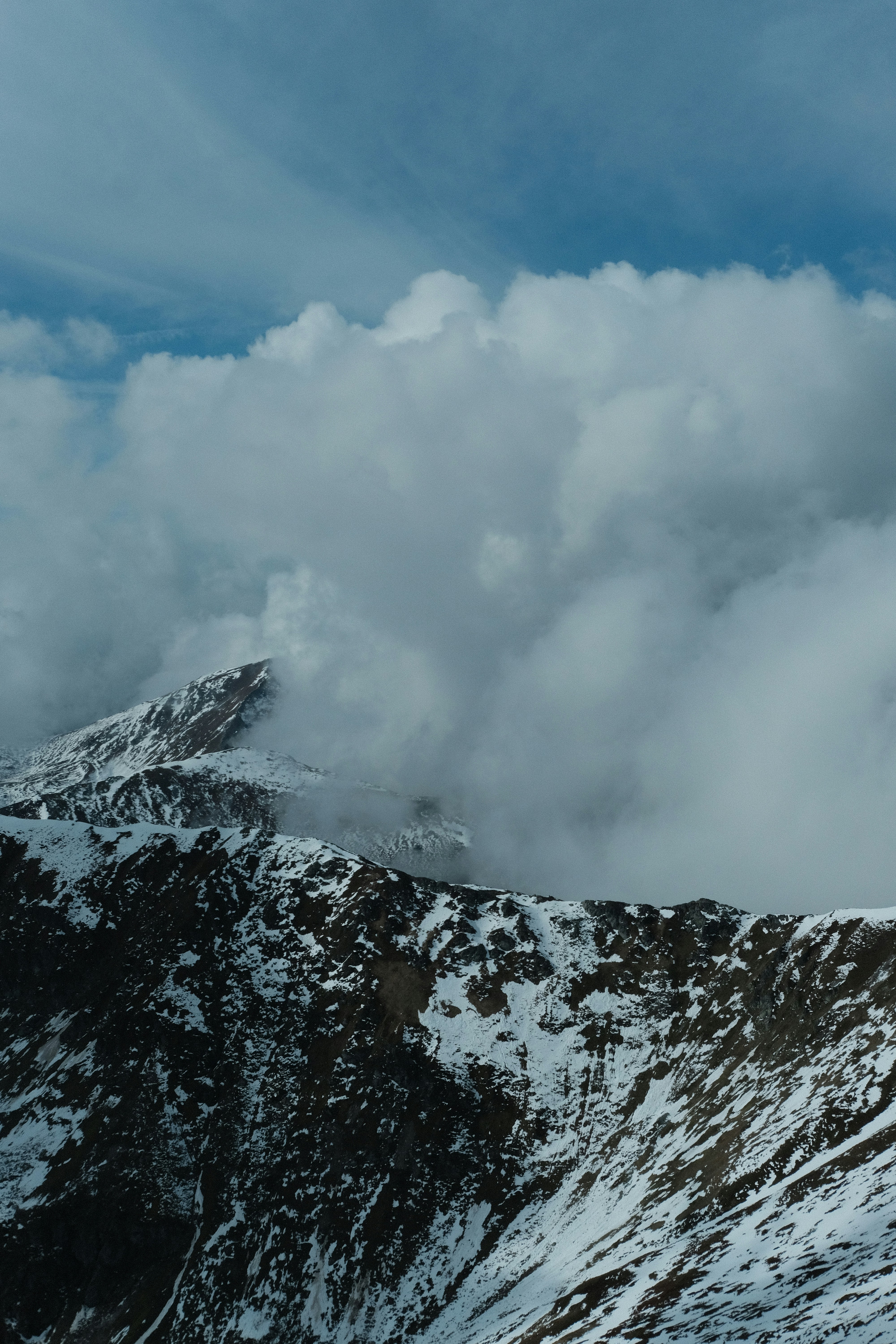 Snowy mountain peaks partially obscured by thick white clouds under a blue sky