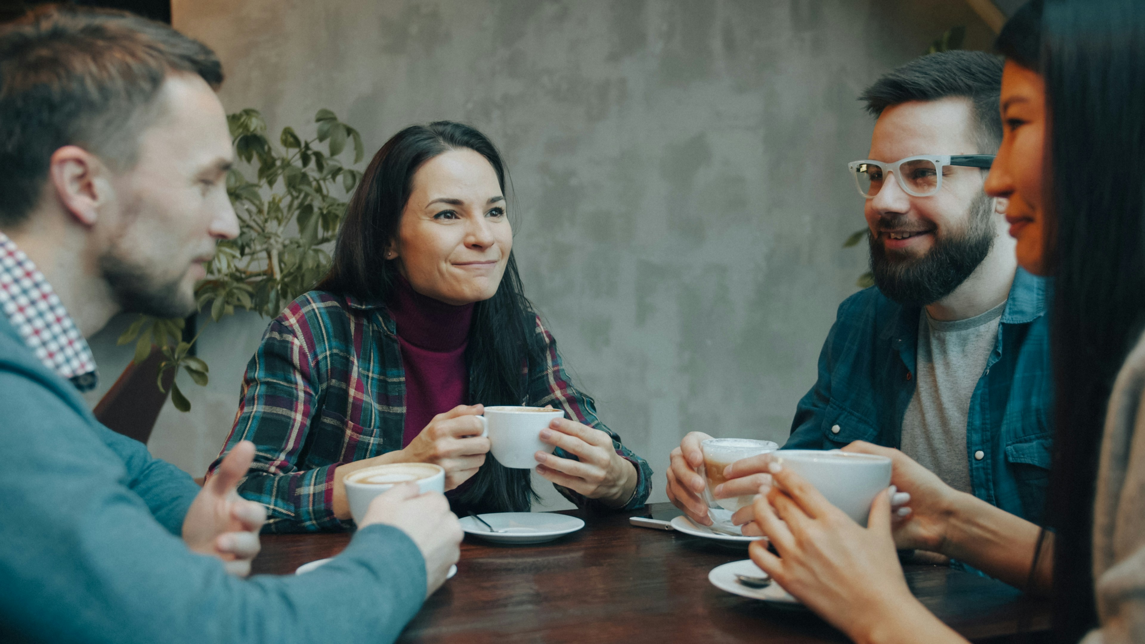 Four friends chatting and laughing over coffee at a wooden table in a community café.