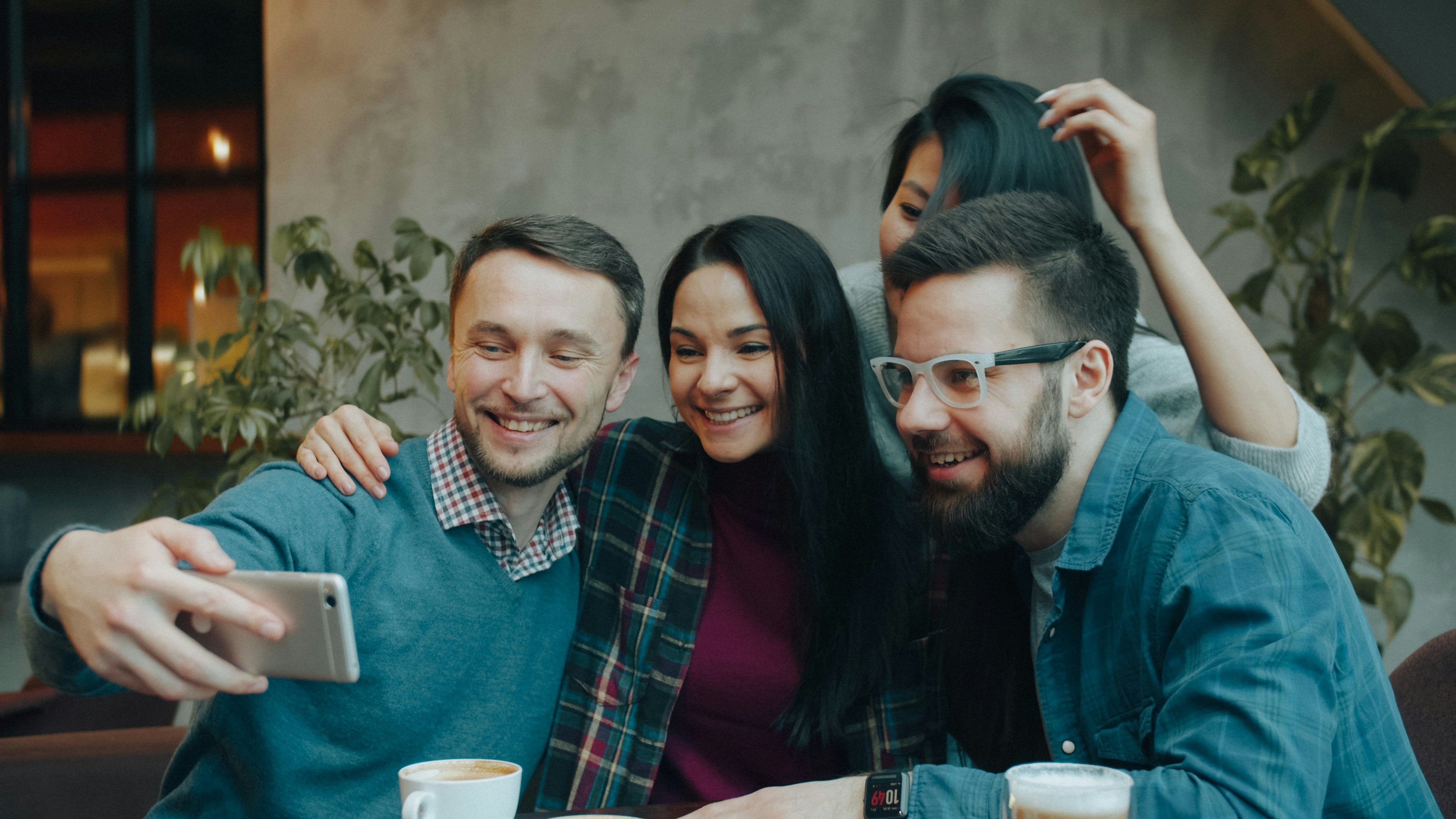 Four friends squeezing together for a selfie at a café table with coffee cups, the playful personal content Meta AI is built for