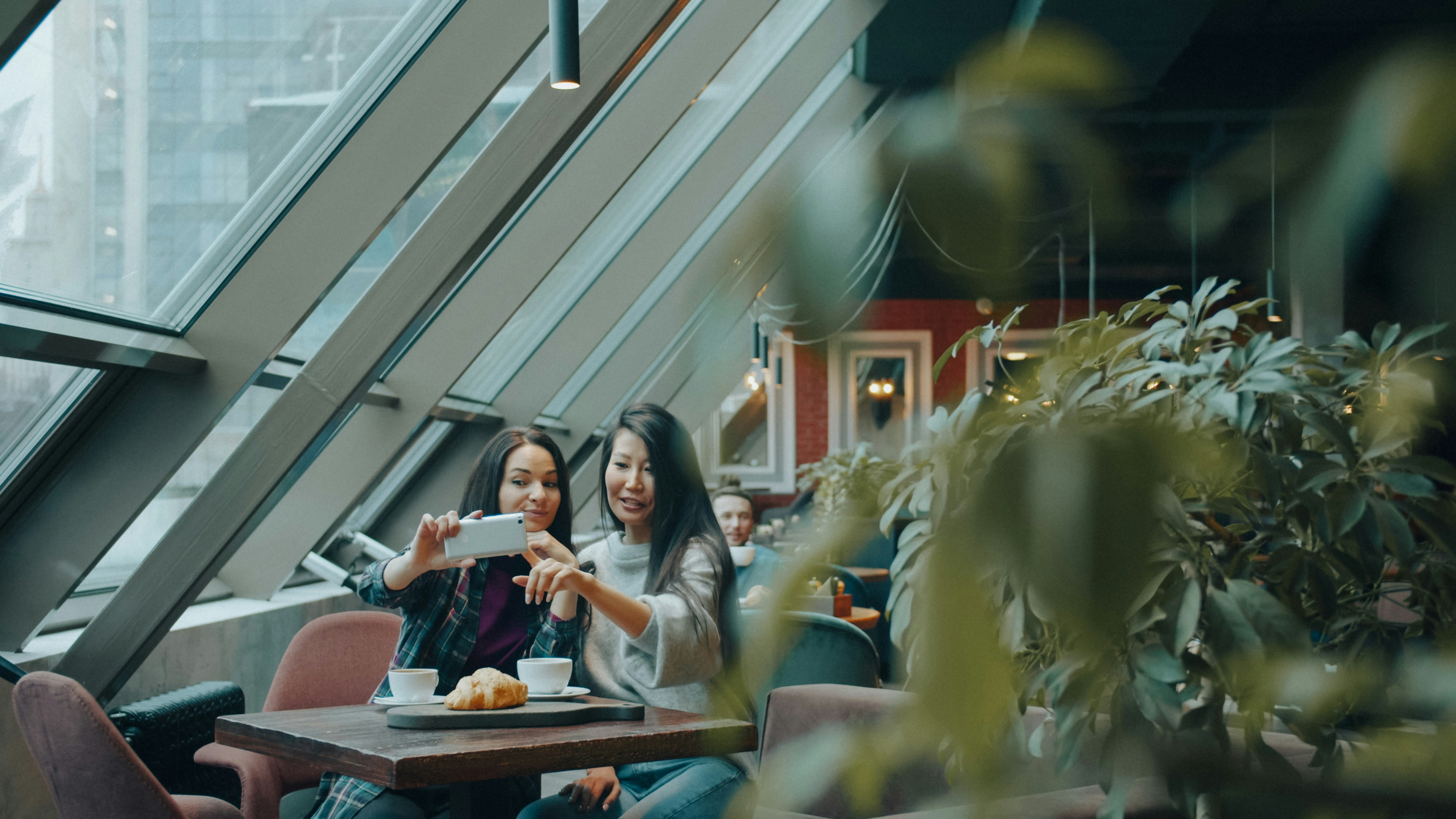 Two women taking a selfie with a smartphone at a cafe table