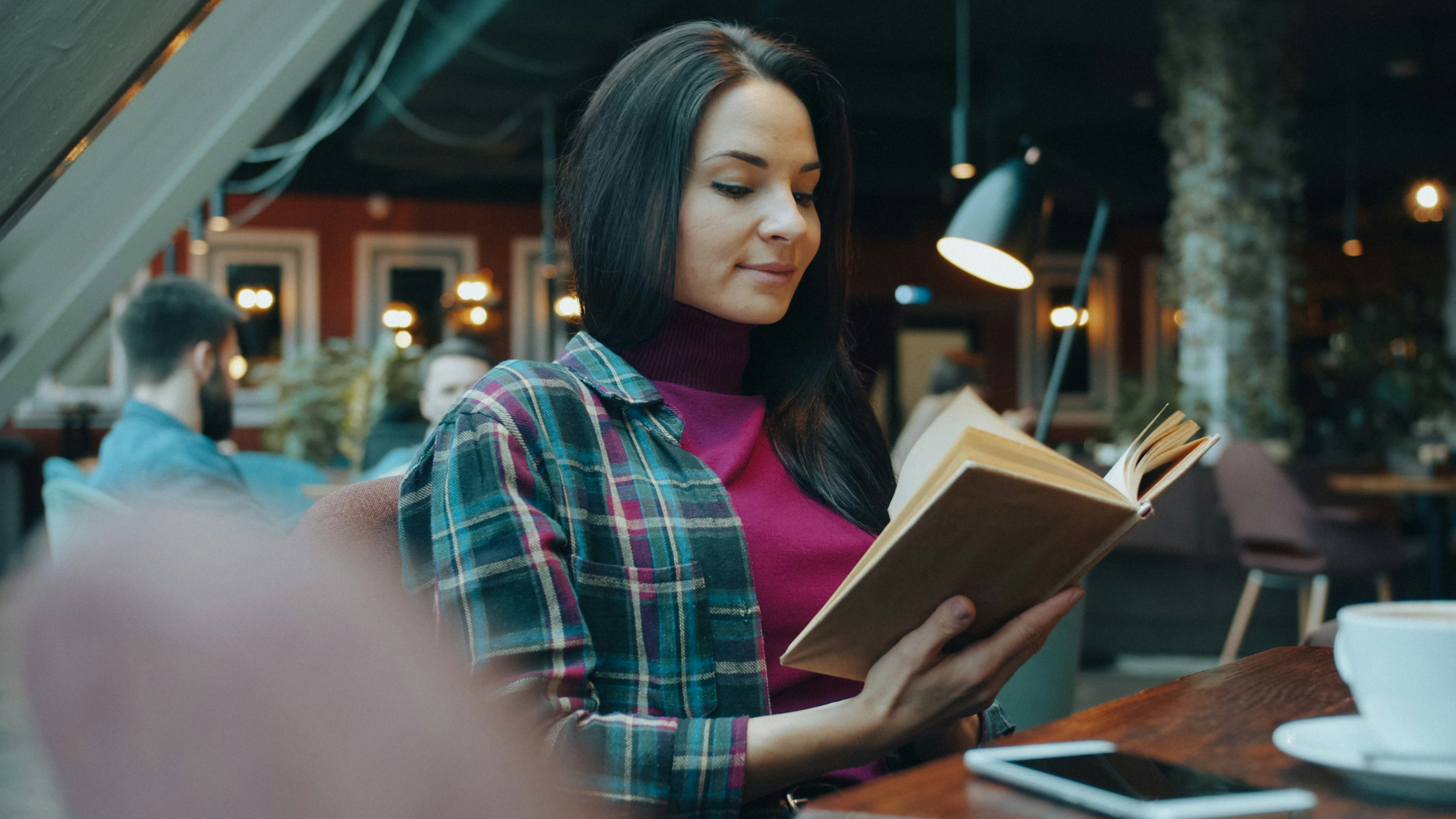 薄暗いカフェでチェック柄のシャツを着た女性が本を読んでいる