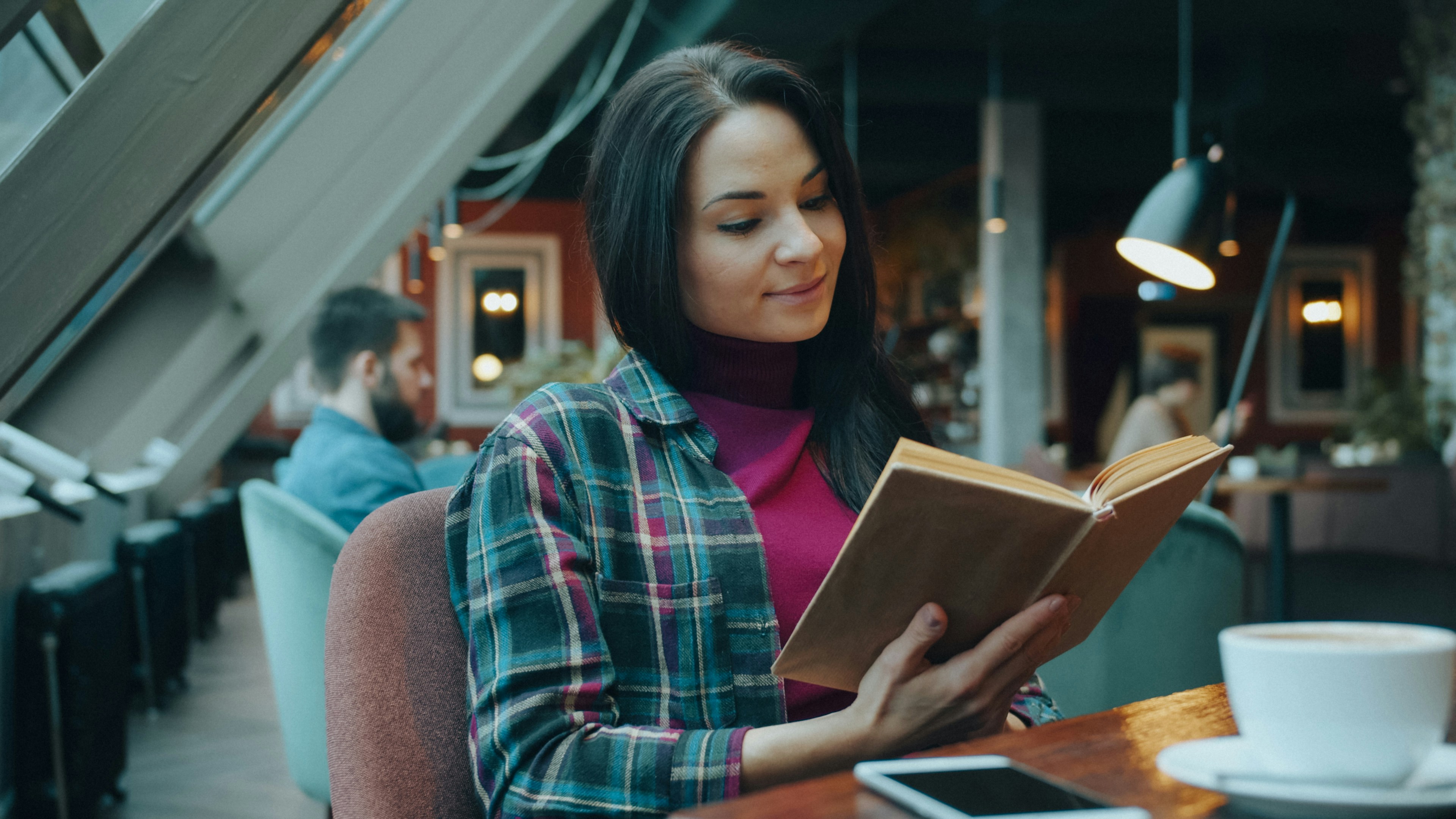 Woman in a plaid shirt reading a book in a cafe