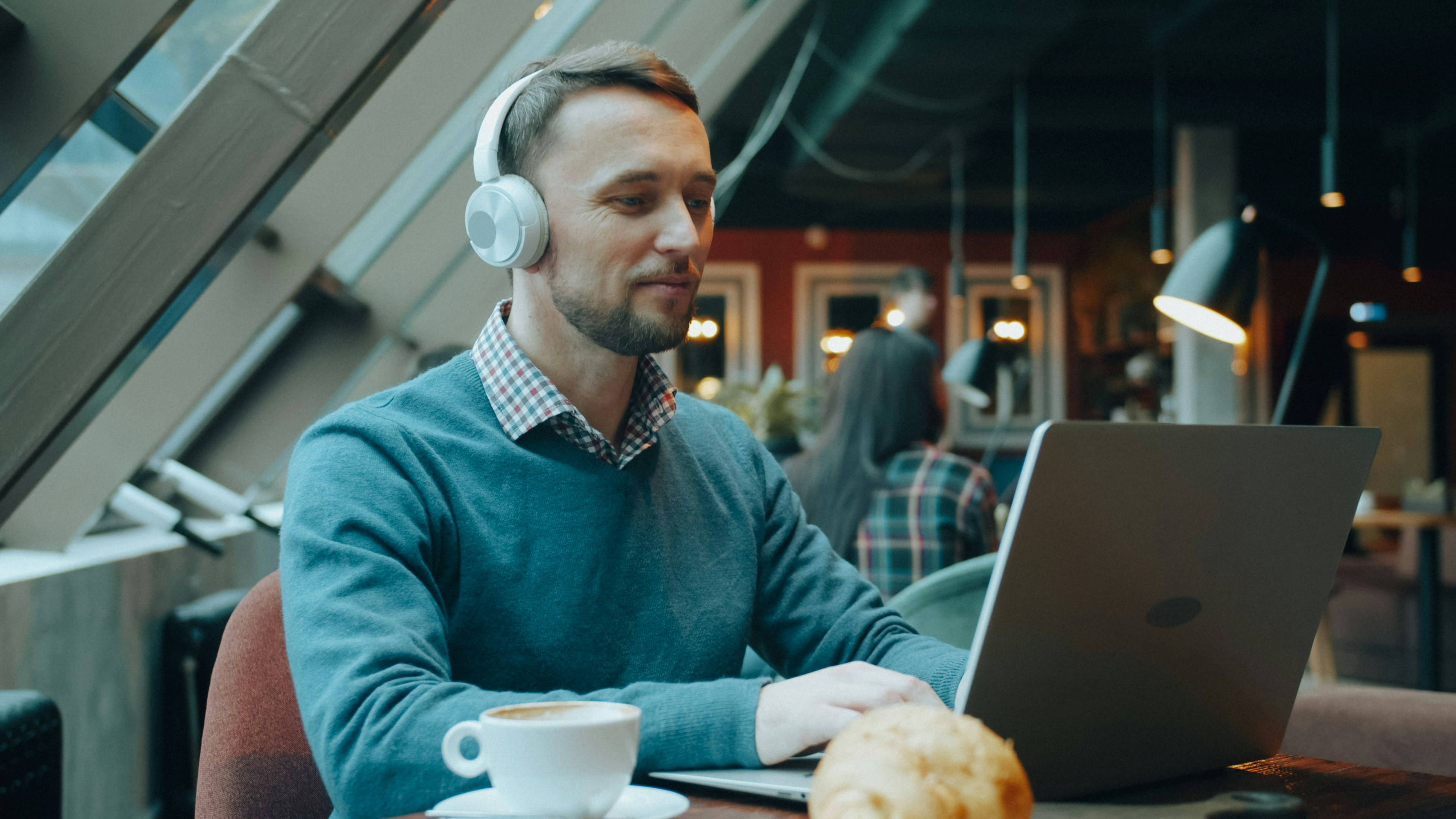 Hombre joven con auriculares trabajando con un portátil en una cafetería