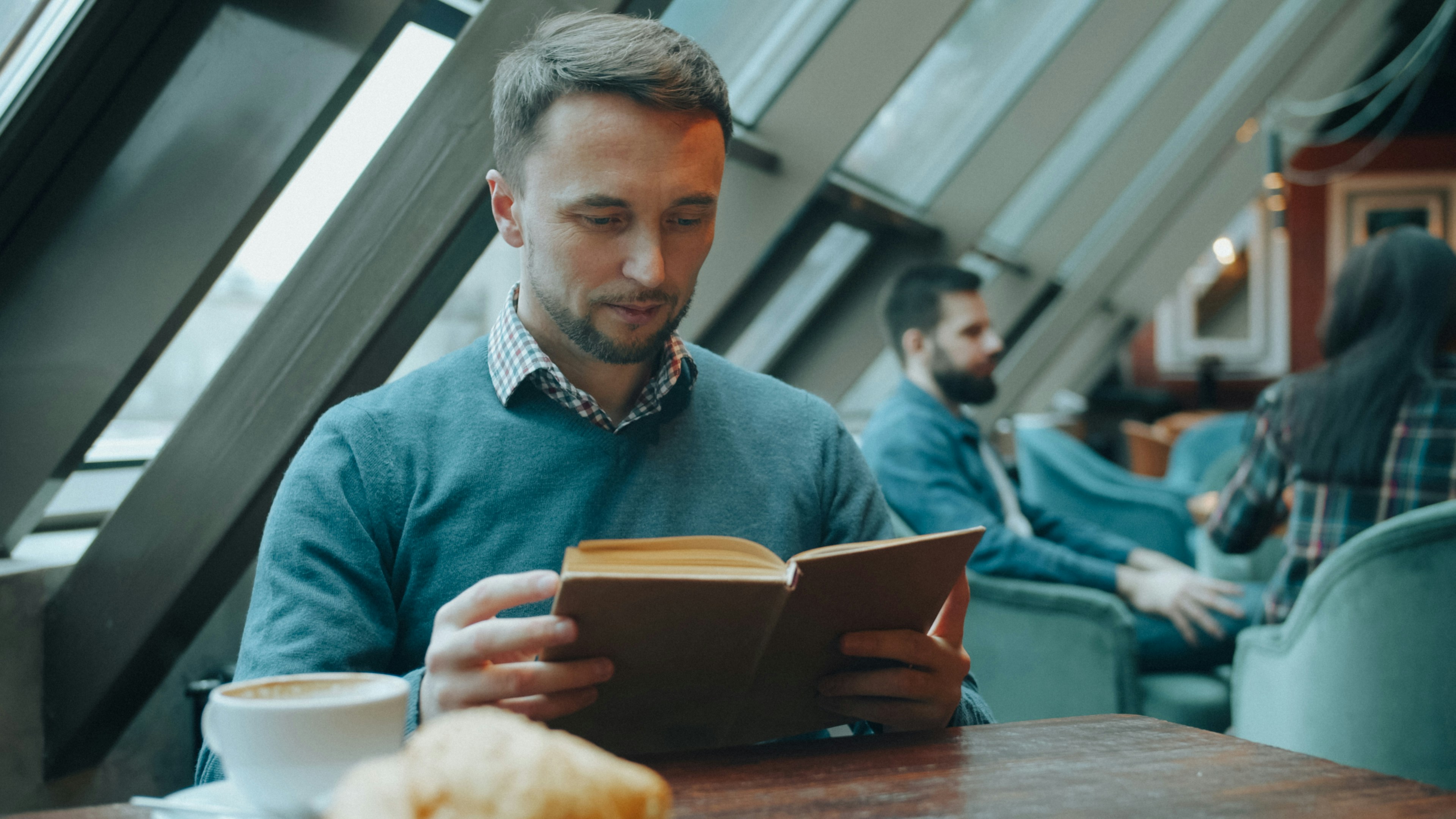 カフェのテーブルでコーヒーを飲みながら本を読んでいる男性