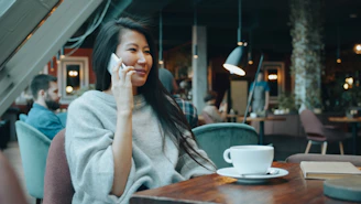 A woman in a grey sweater talking on a phone in a cafe