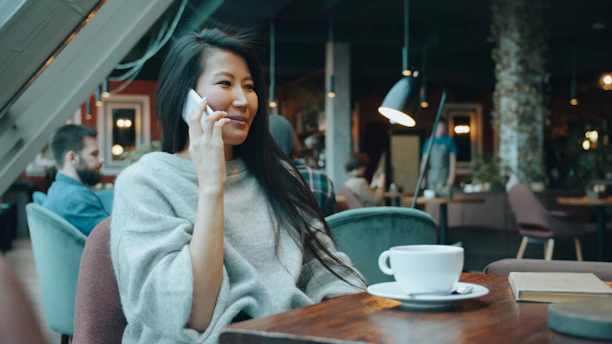 A woman in a grey sweater talking on a phone in a cafe
