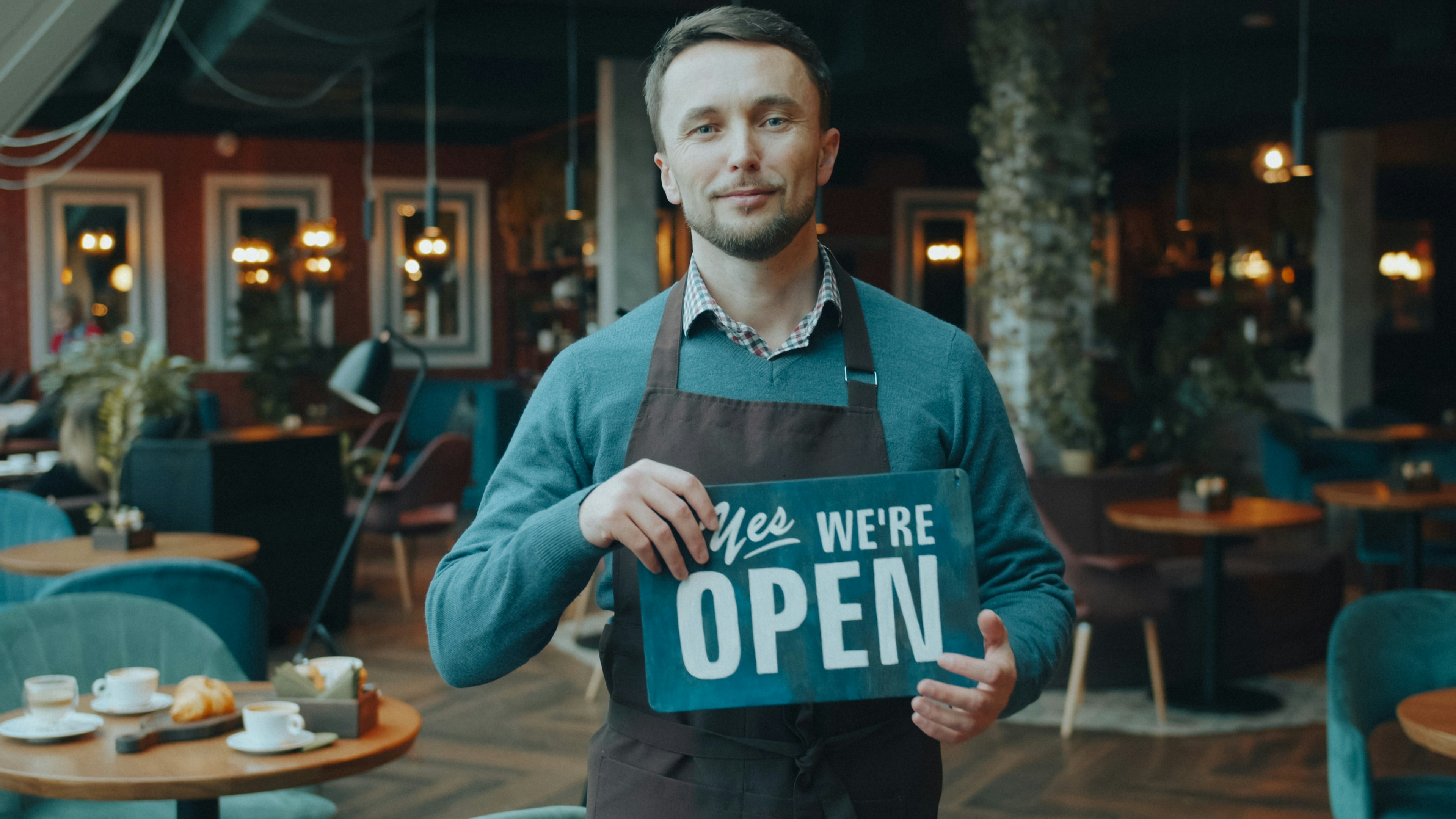 A man in a brown apron holding a sign reading 