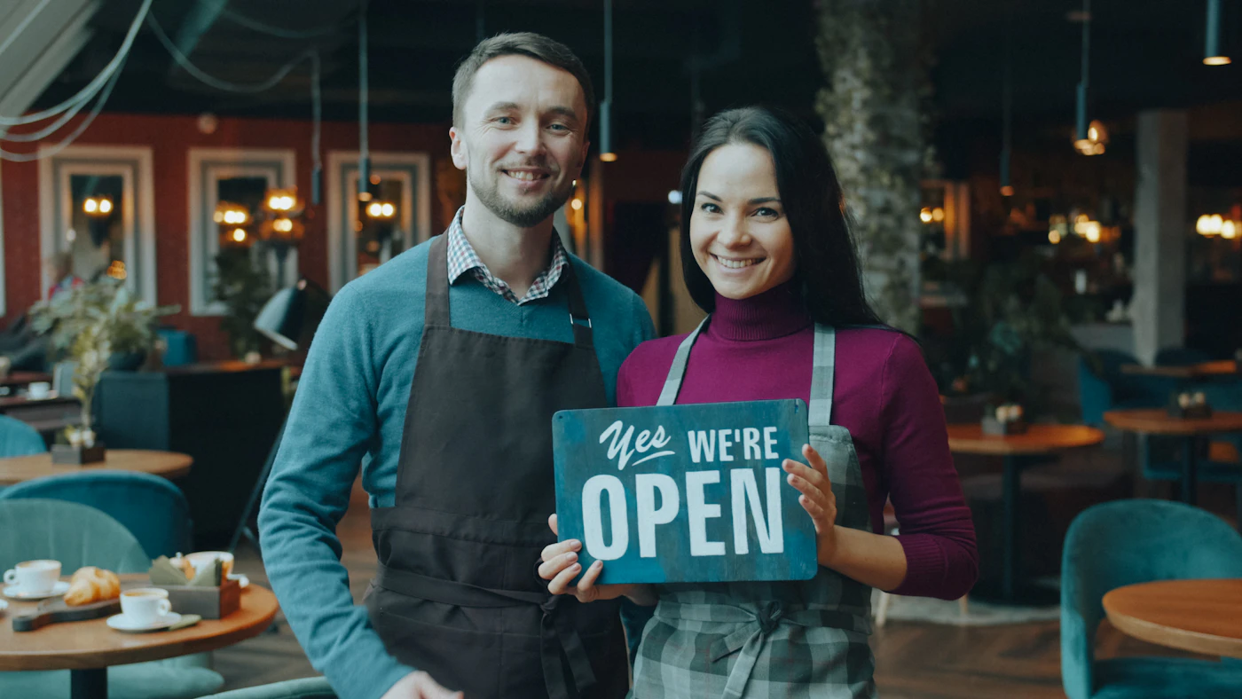 Restaurant owners in aprons holding a sign that says Yes, we're open