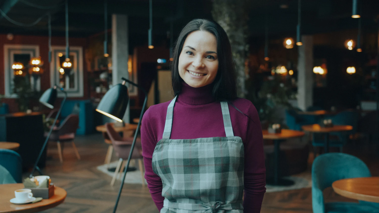 A woman in a plaid apron standing in a dimly lit dining room