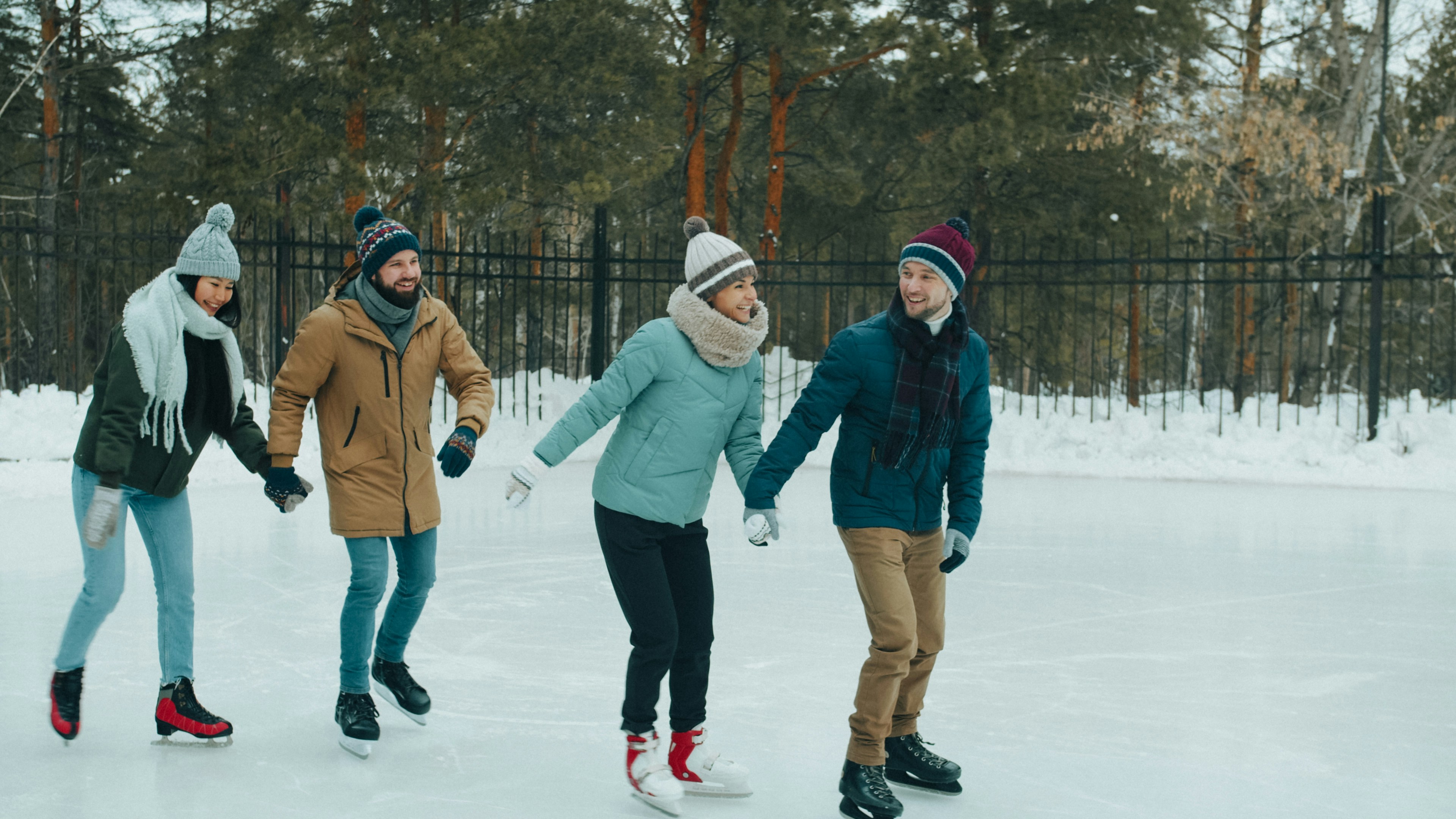 Four people holding hands while ice skating on an outdoor rink in winter