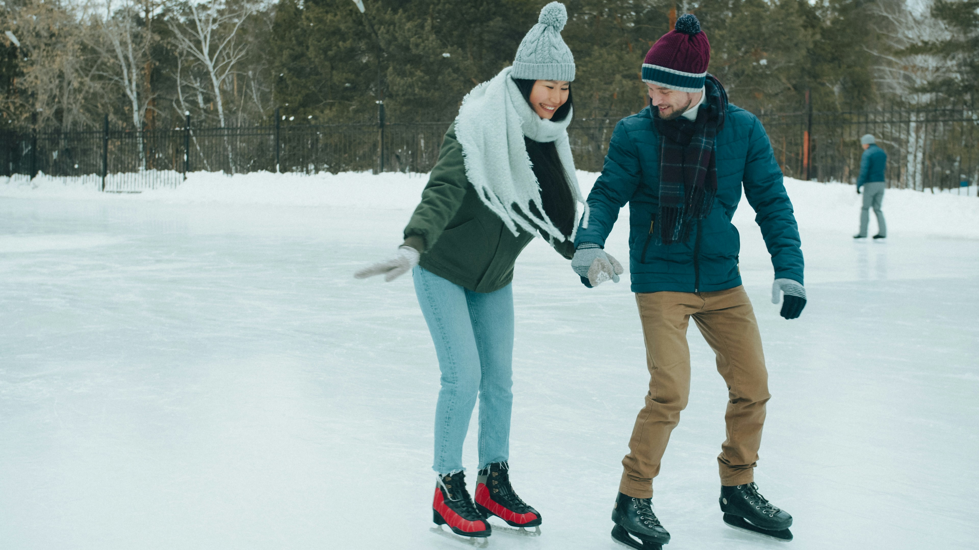 A woman and a man ice skating together on an outdoor rink