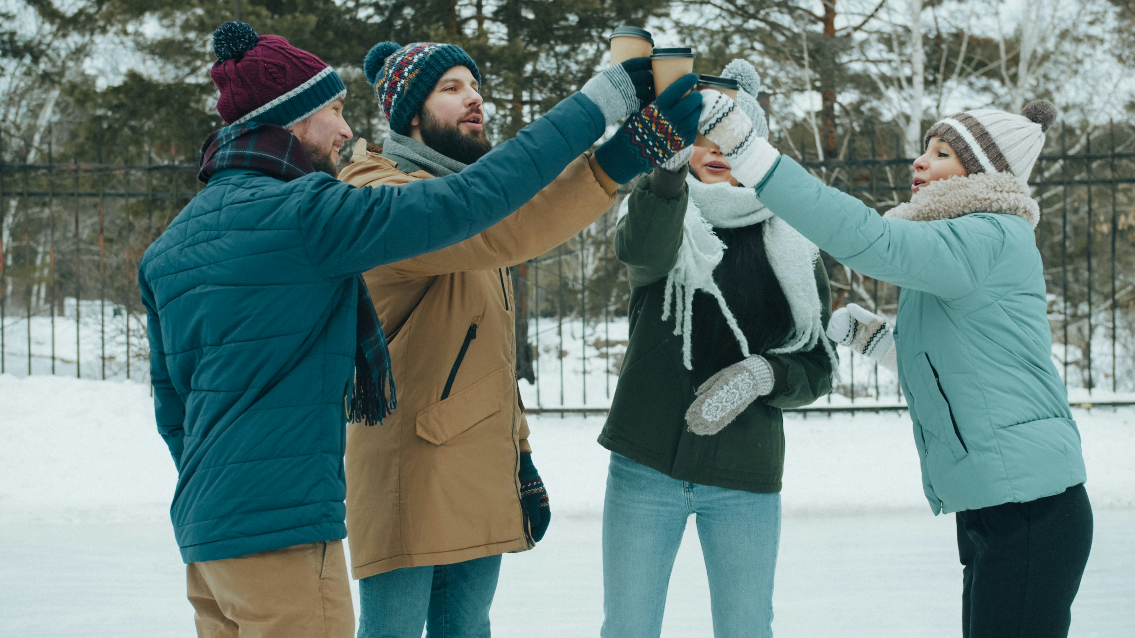 Four people in winter clothing toasting with paper coffee cups on a snowy day