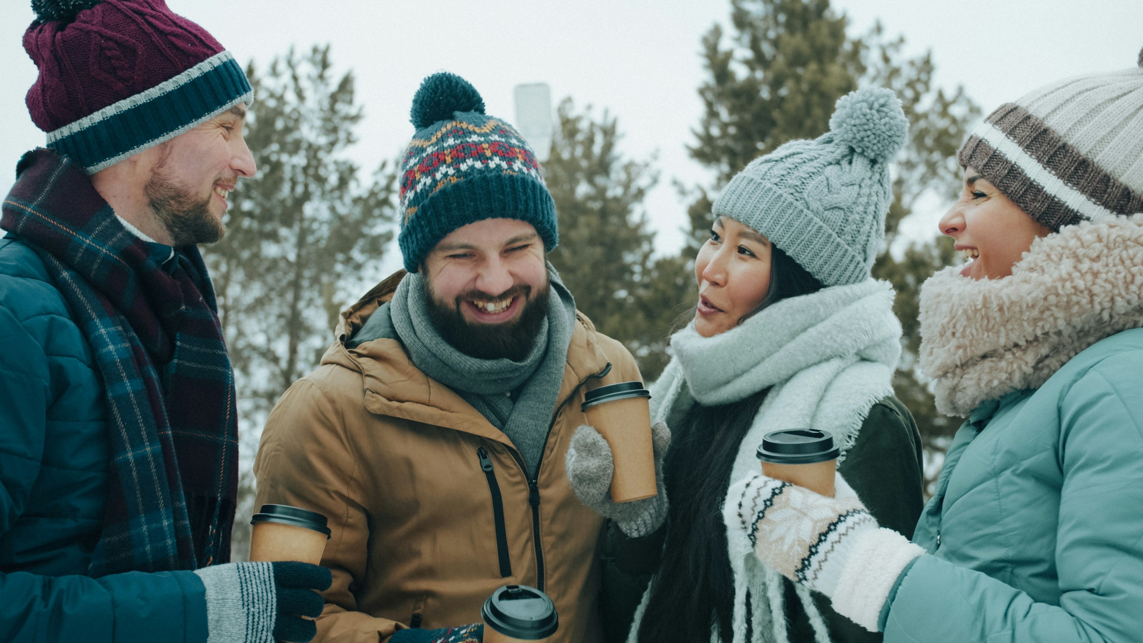 A group of four people in winter clothing holding coffee cups outdoors