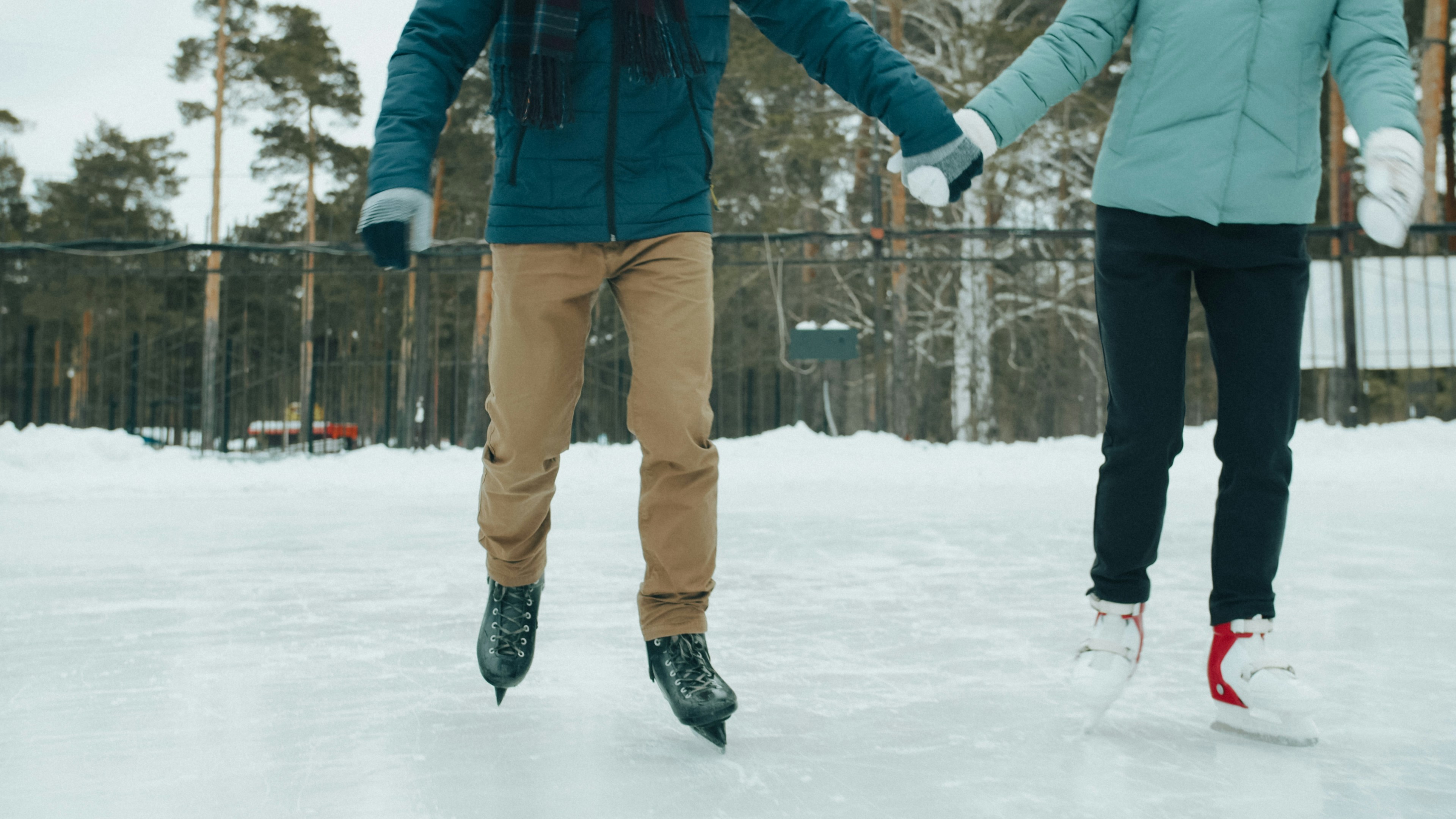 Two people holding hands while ice skating on an outdoor rink in winter