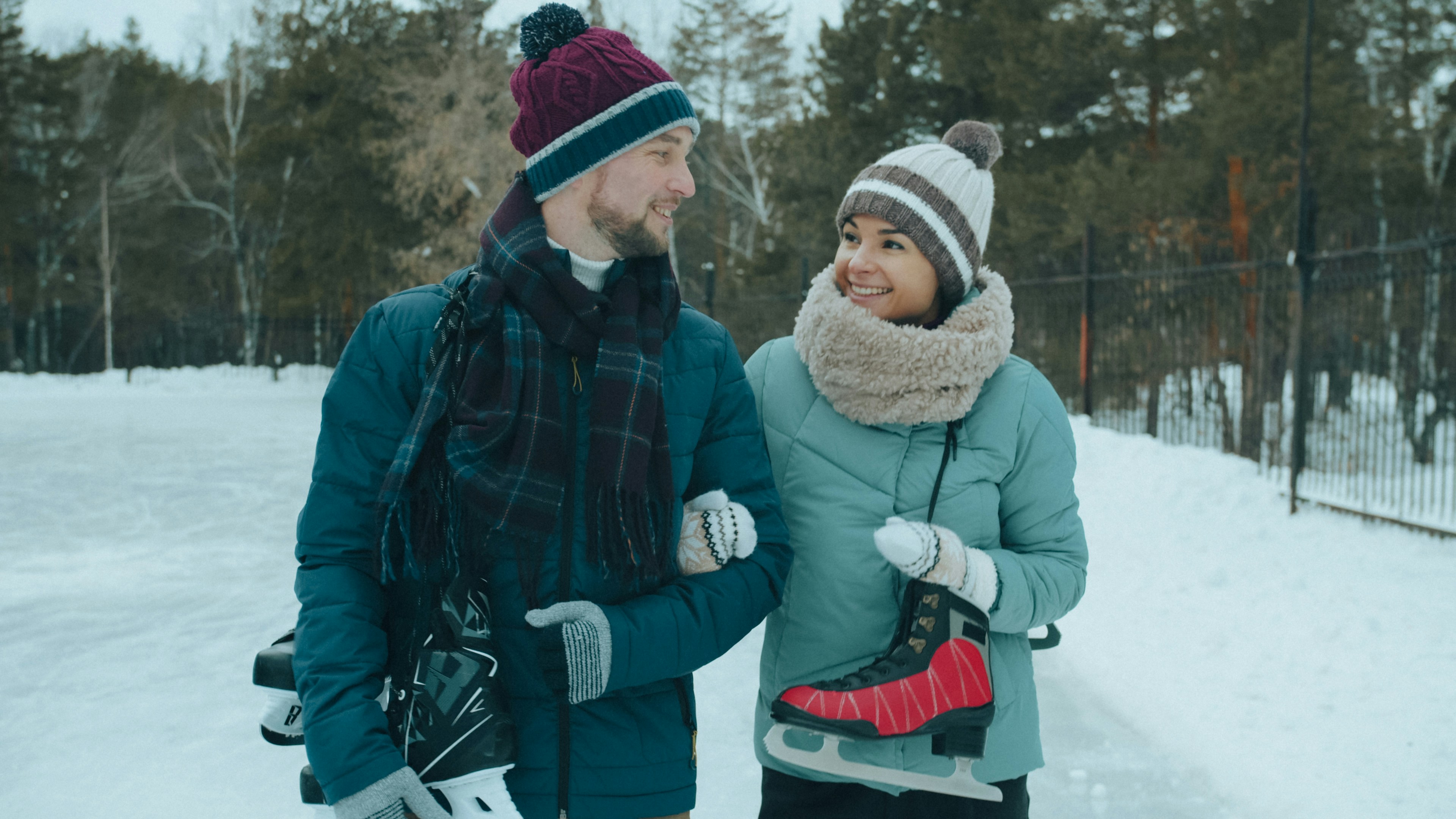 A man and a woman in winter gear carrying ice skates on a rink