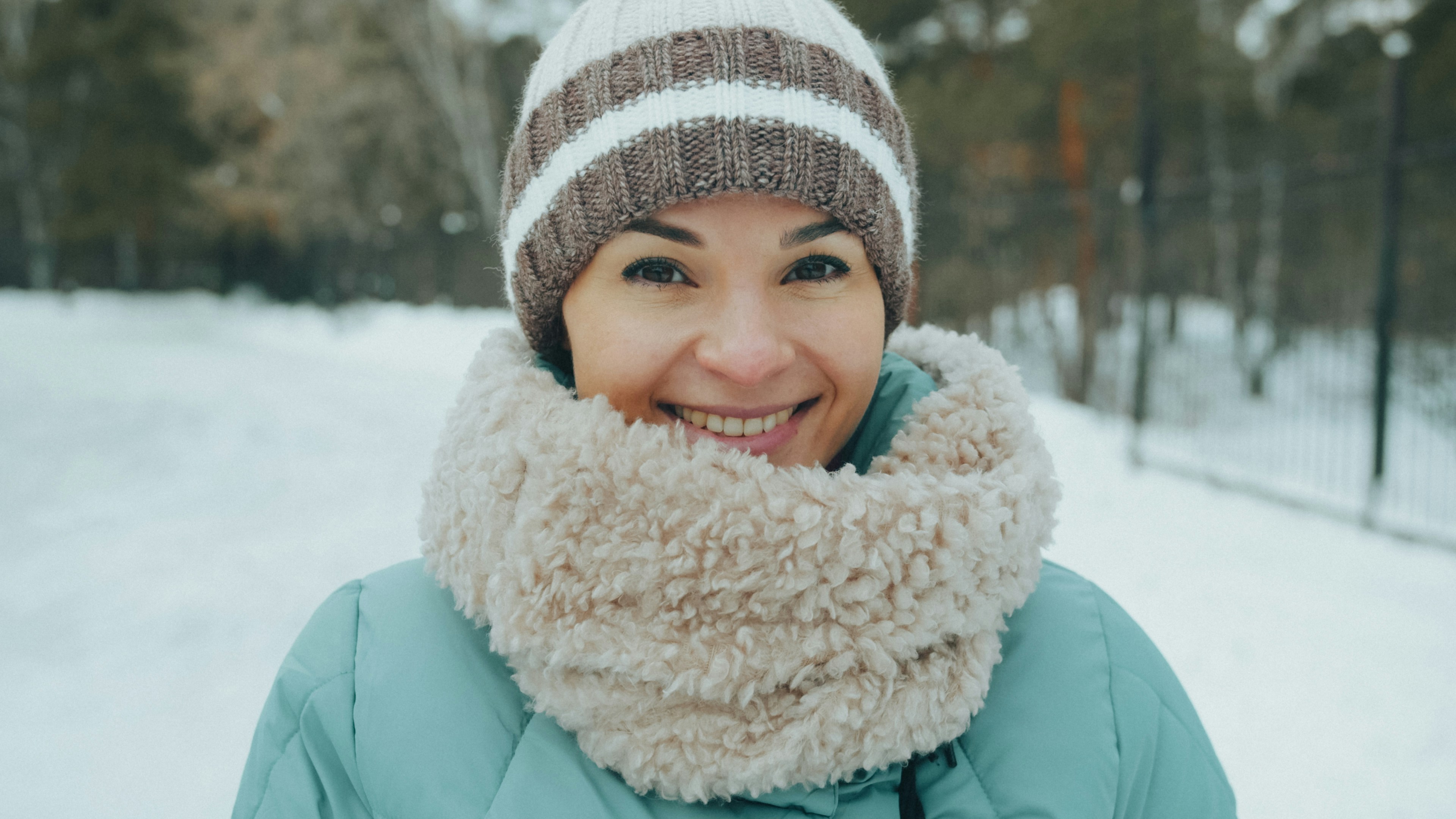 A smiling woman wearing a knit beanie and a fluffy scarf in winter
