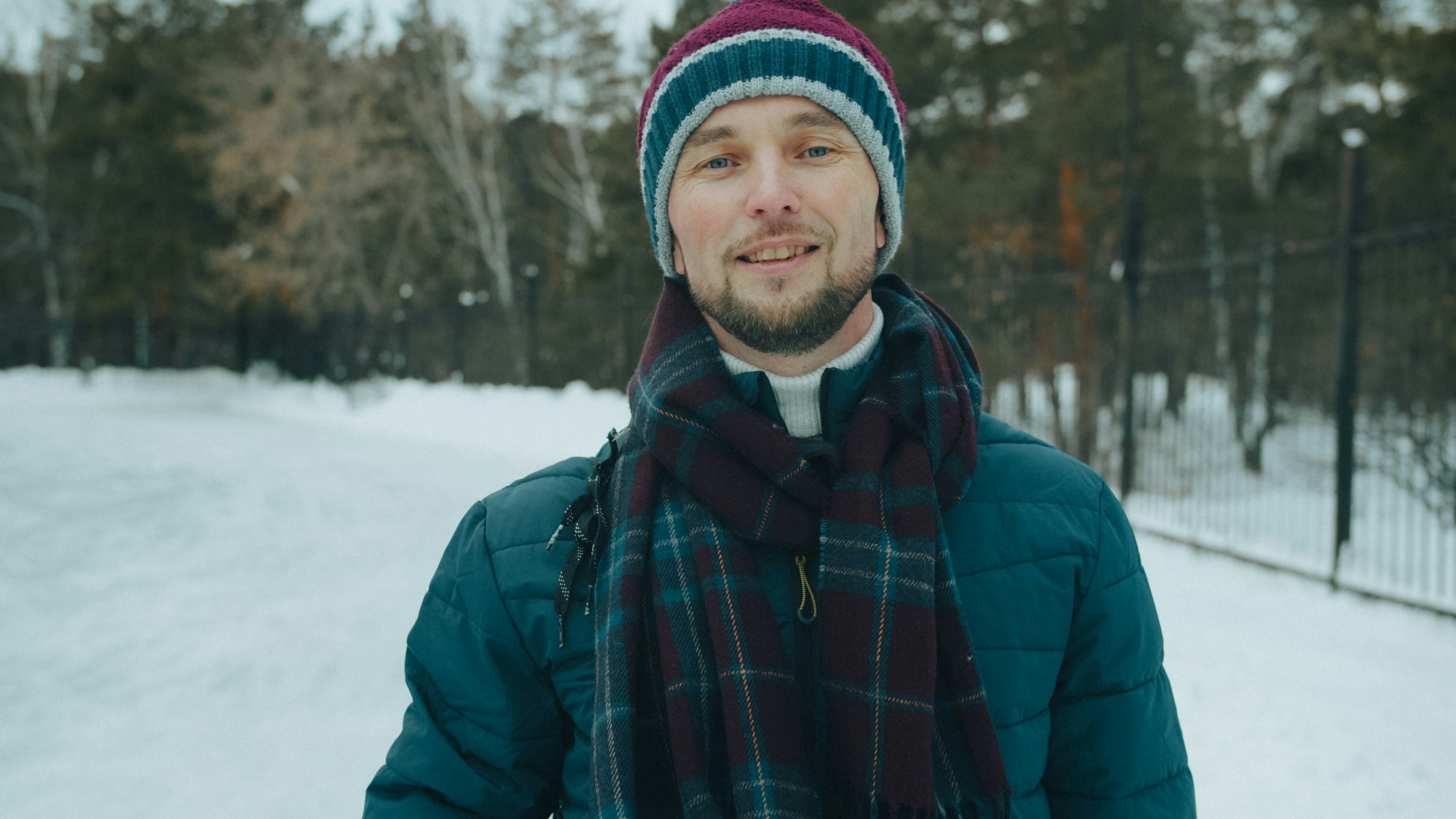 A man in a teal puffer jacket and plaid scarf in a snowy park