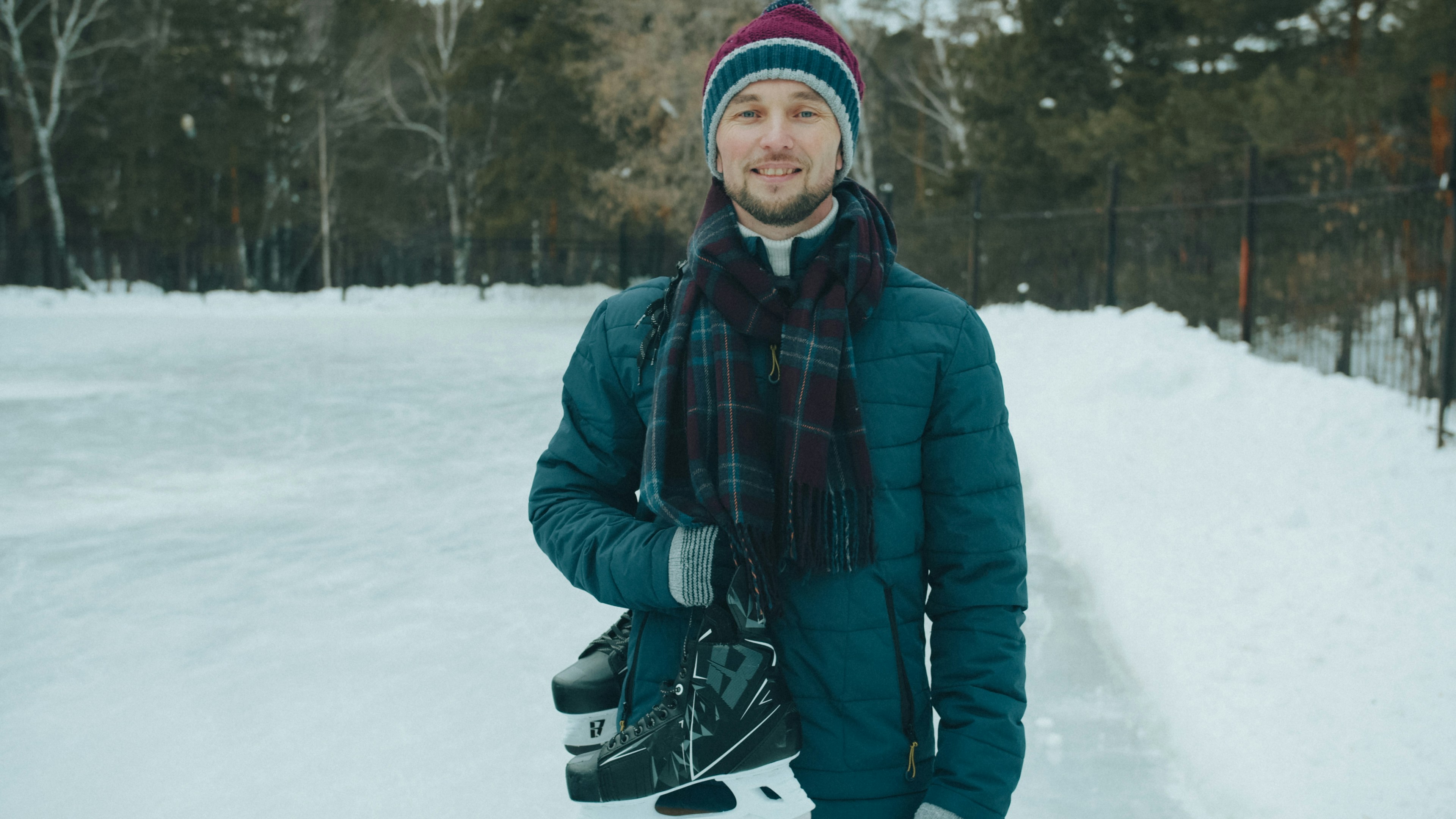 A man in winter clothes holding ice skates at an outdoor rink