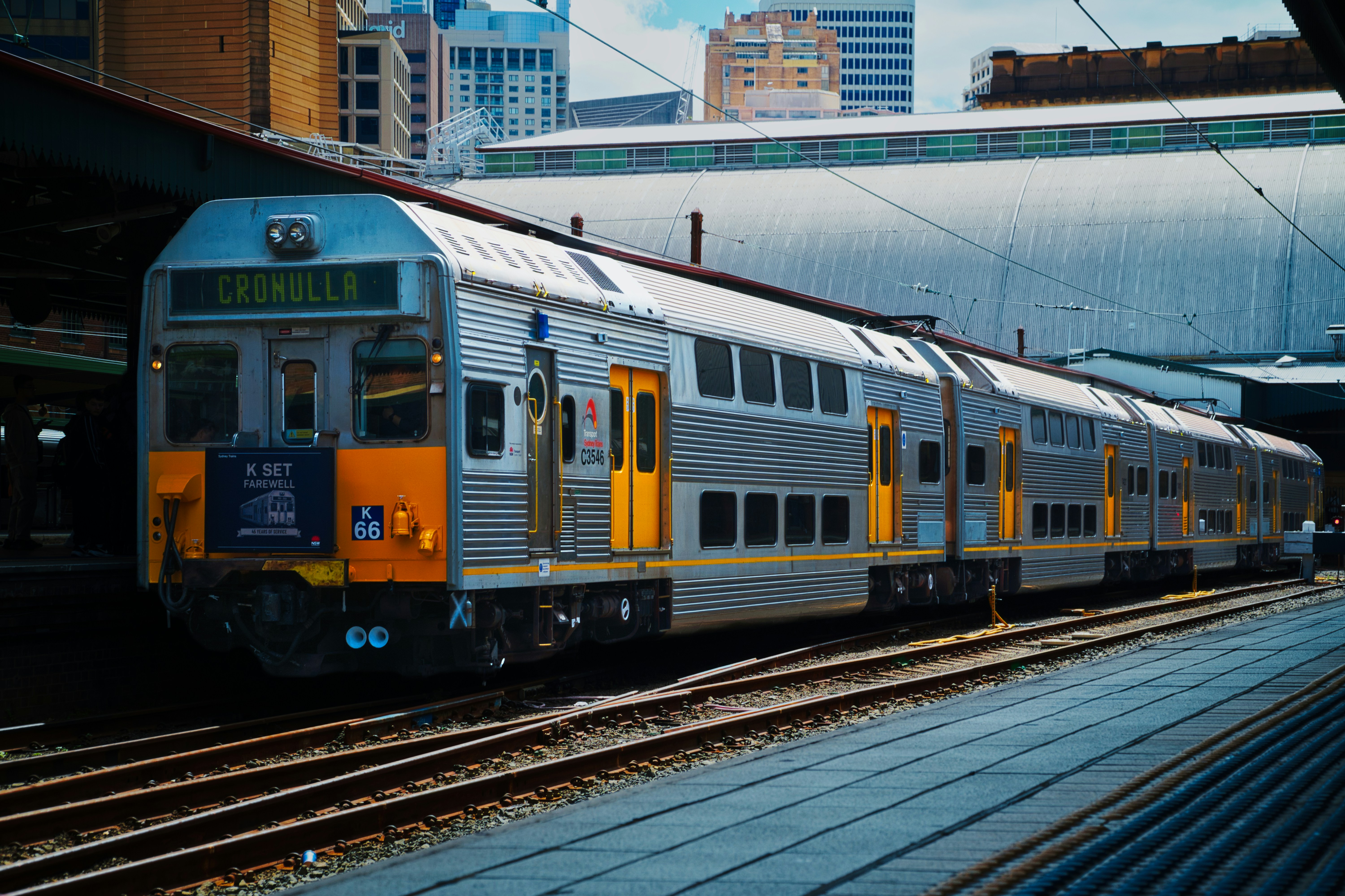 A silver double-decker train at a station platform with a sign reading Cronulla
