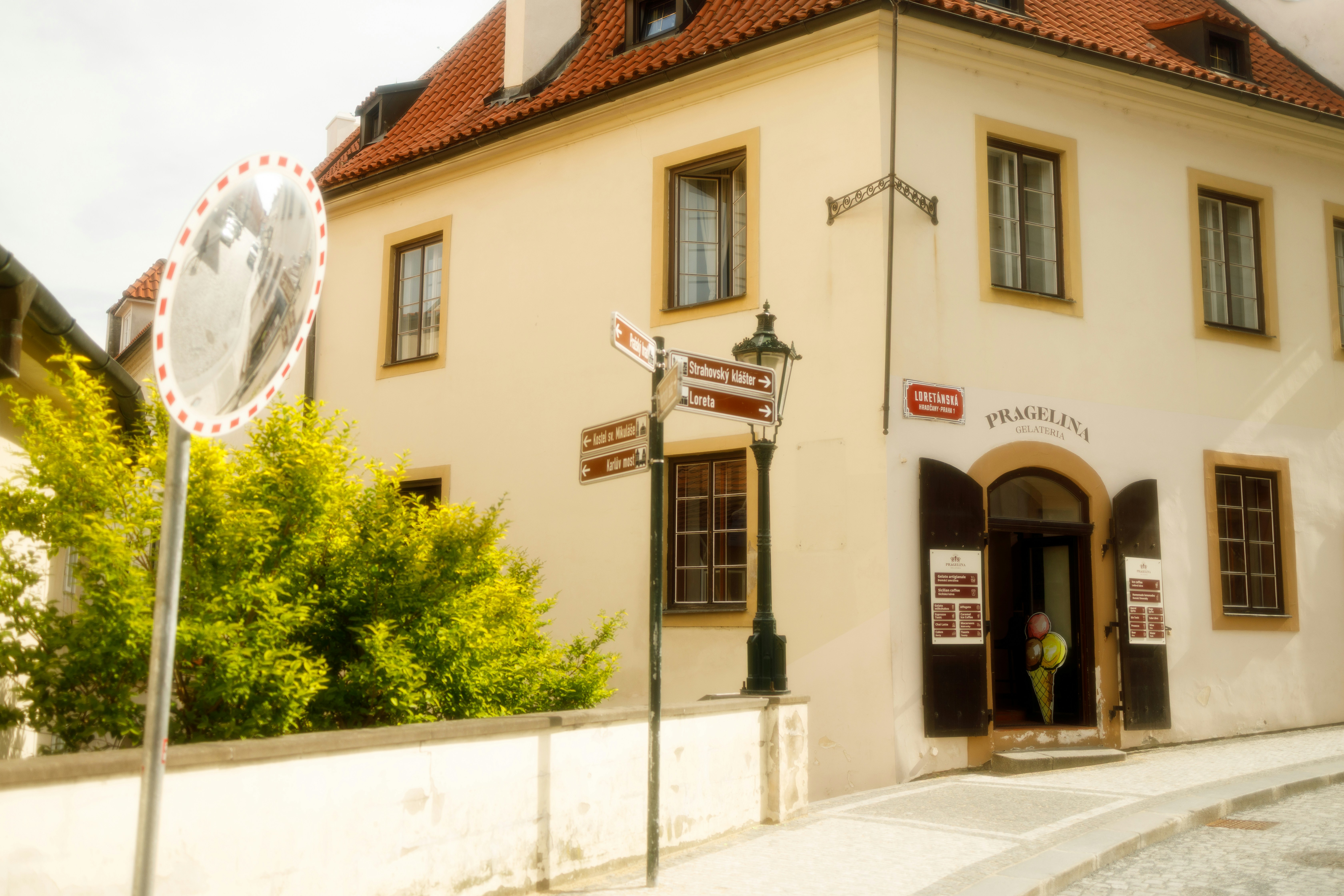 A street corner with a cream building, directional signs, and a convex mirror in Prague