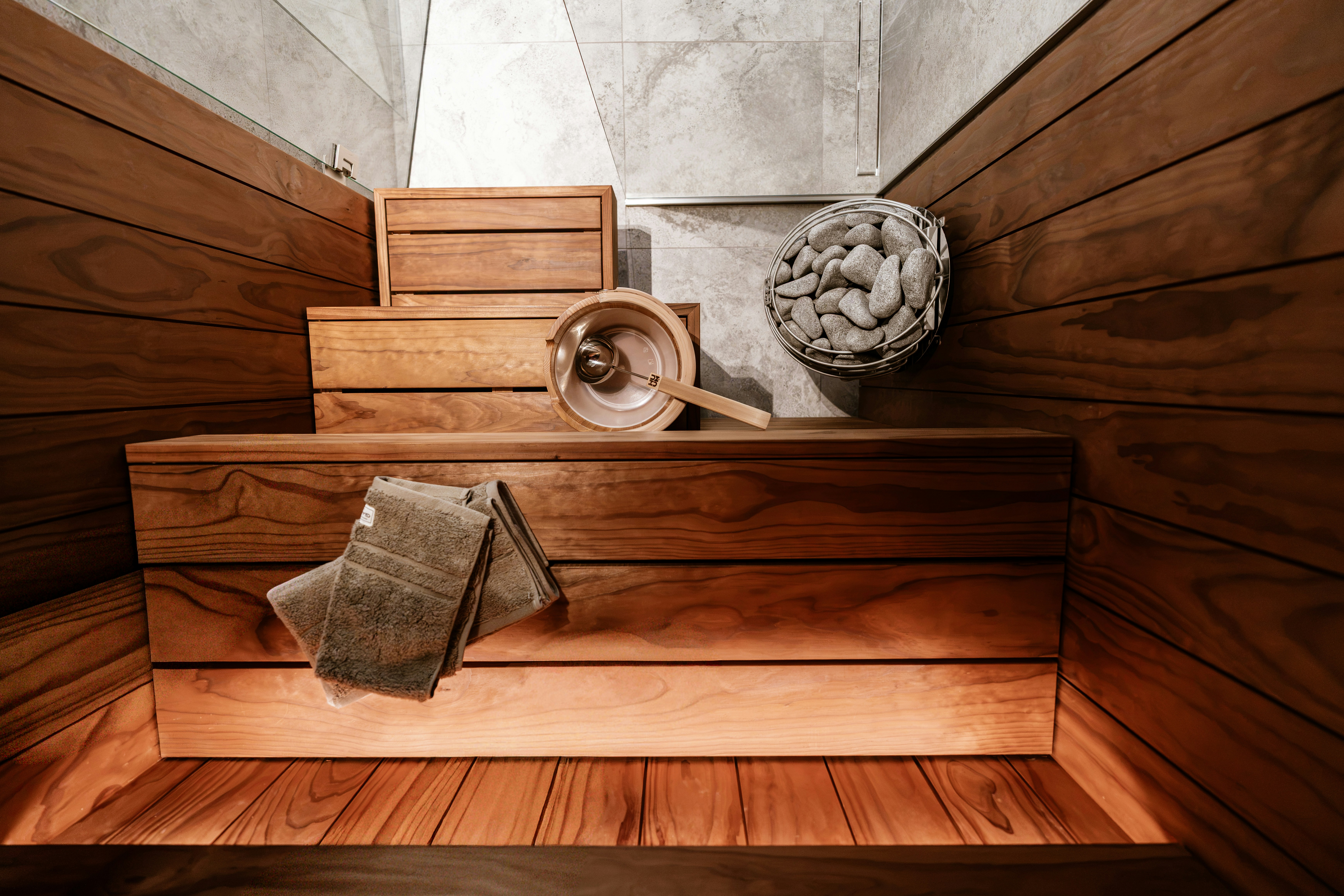 A wooden sauna interior with a bucket, ladle, stones, and folded towels