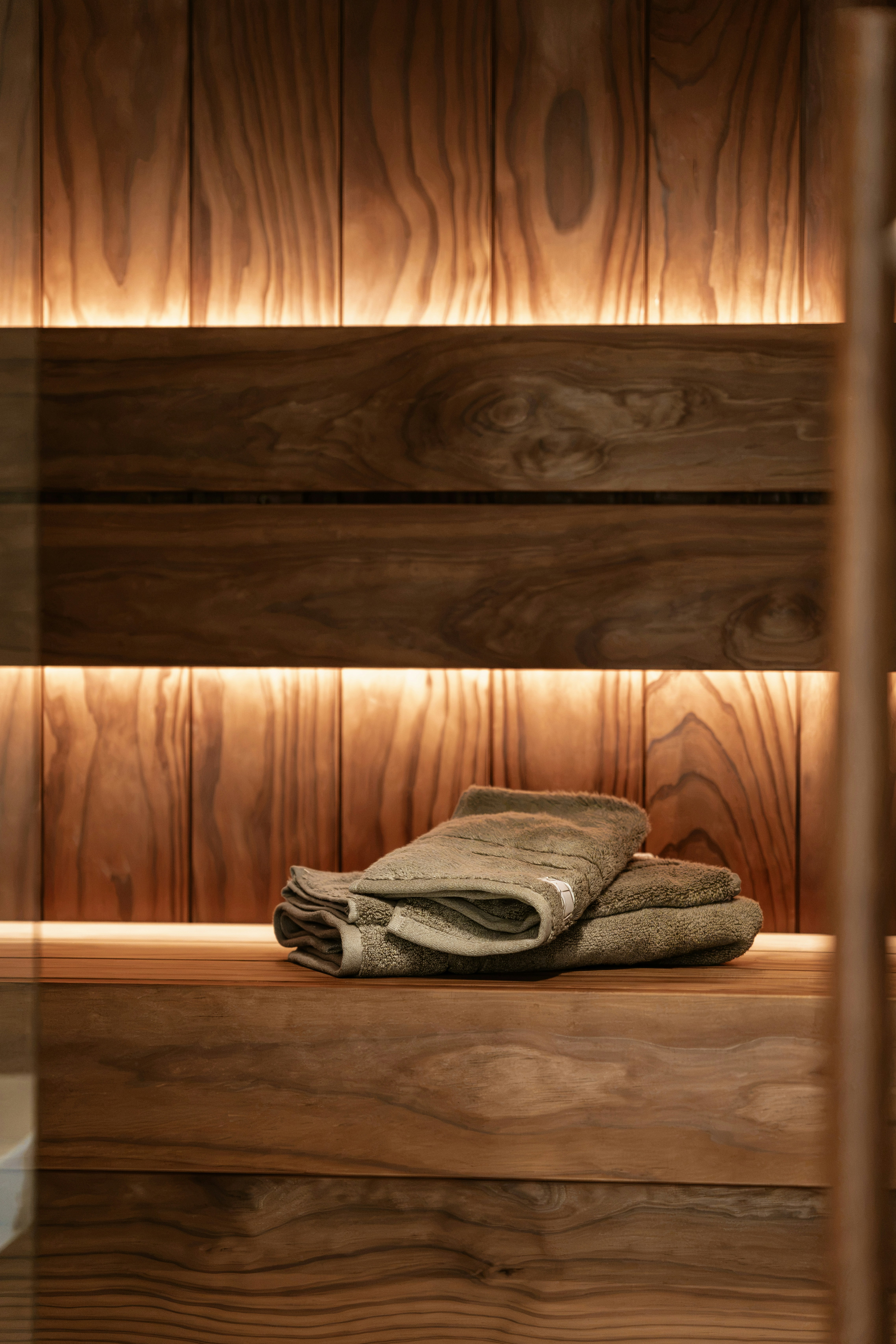 Folded grey towels on a wooden bench in a sauna with warm lighting