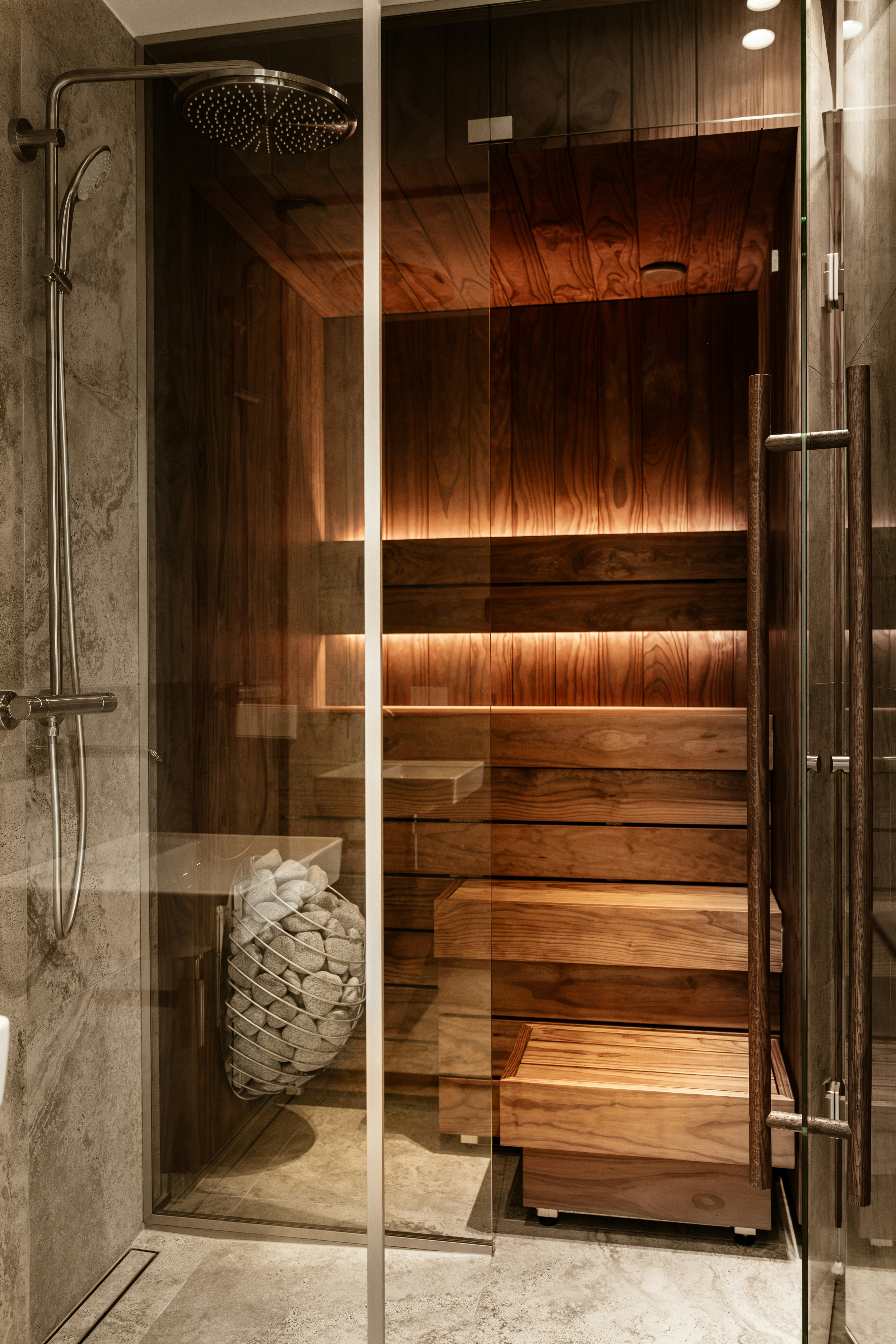 A glass shower enclosure beside a wooden sauna with tiered benches and warm lighting