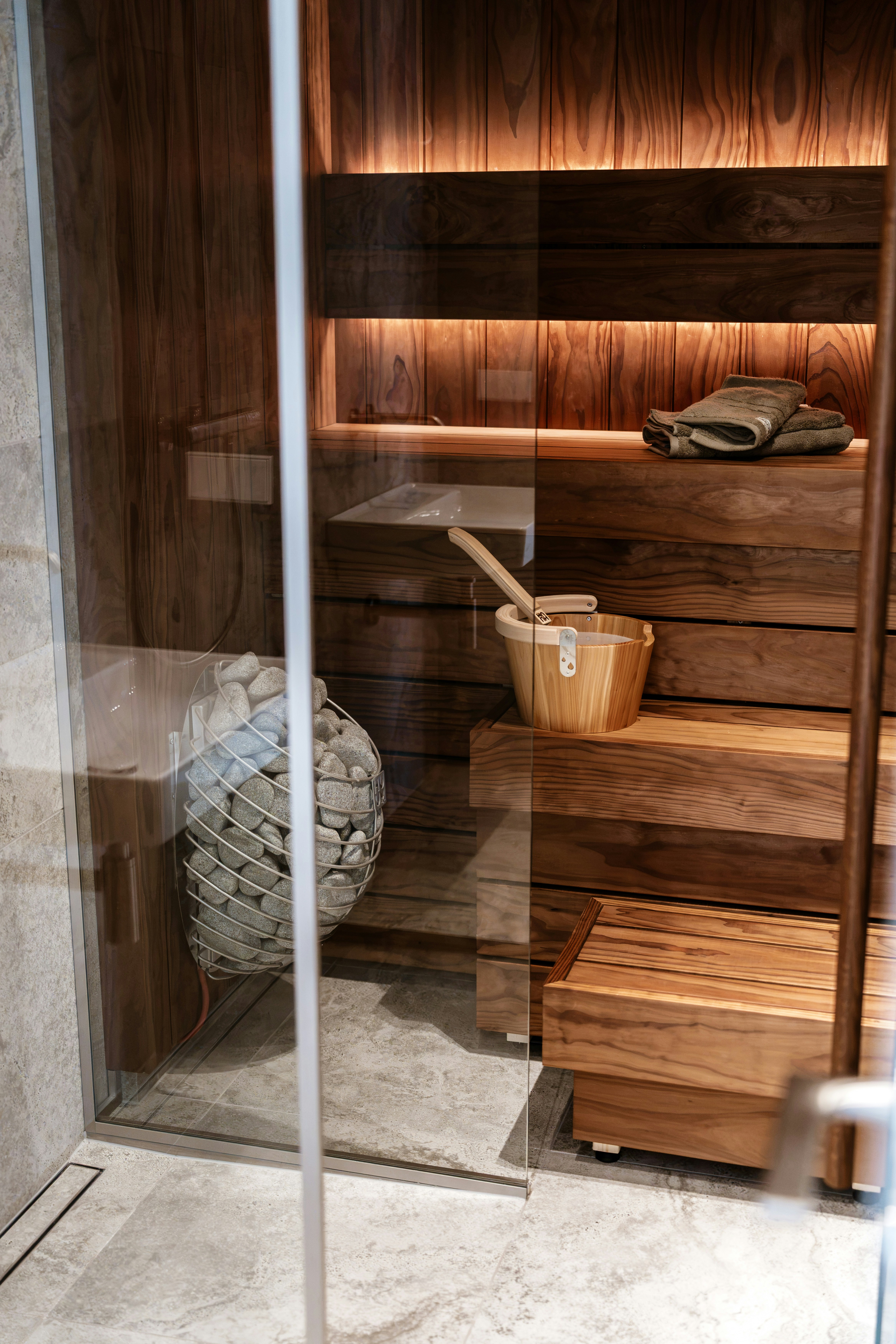 A wooden sauna interior with a bucket, stones in a cage, and towels